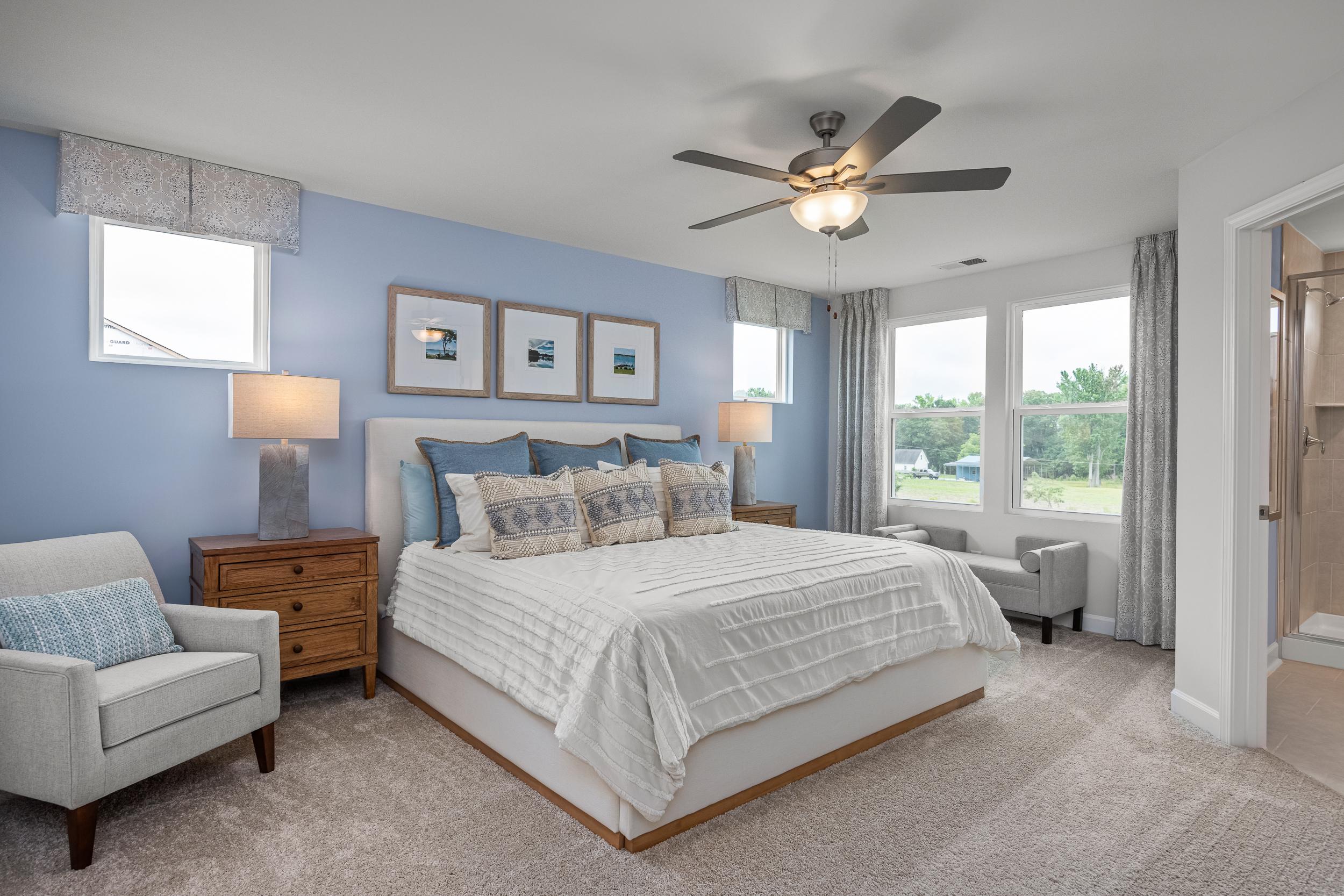Spacious primary bedroom in Springvale Fuquay-Varina NC with blue walls king bed ceiling fan and large windows by Davidson Homes