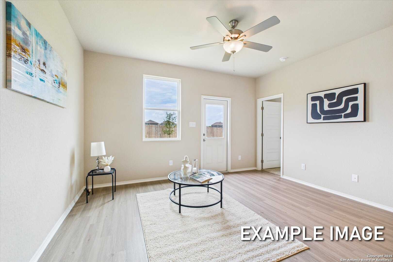 Bright living room with ceiling fans, abstract wall art, wood floors, and French doors in Davidson Homes Comal B, Agave, San Antonio