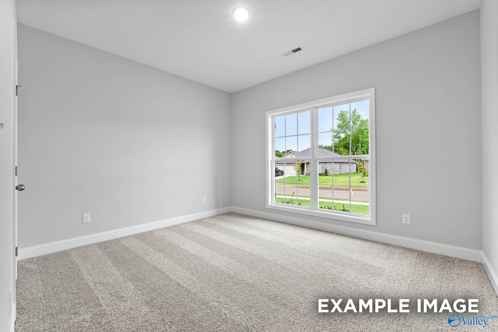 Bright empty bedroom with gray walls, beige carpet, and large window overlooking green yard in The Daphne 4-bedroom home, Meridianville, Alabama