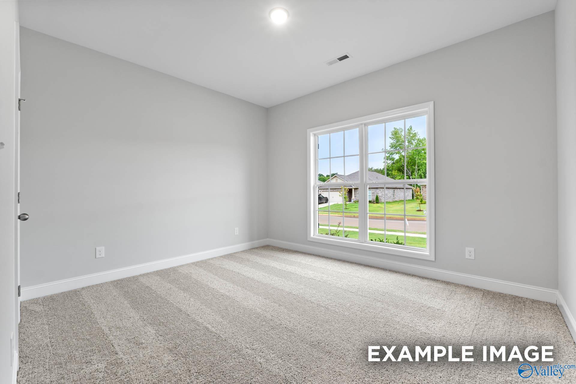 Bright empty bedroom with gray walls, beige carpet, and large window overlooking neighborhood in The Daphne home, Meridianville, AL