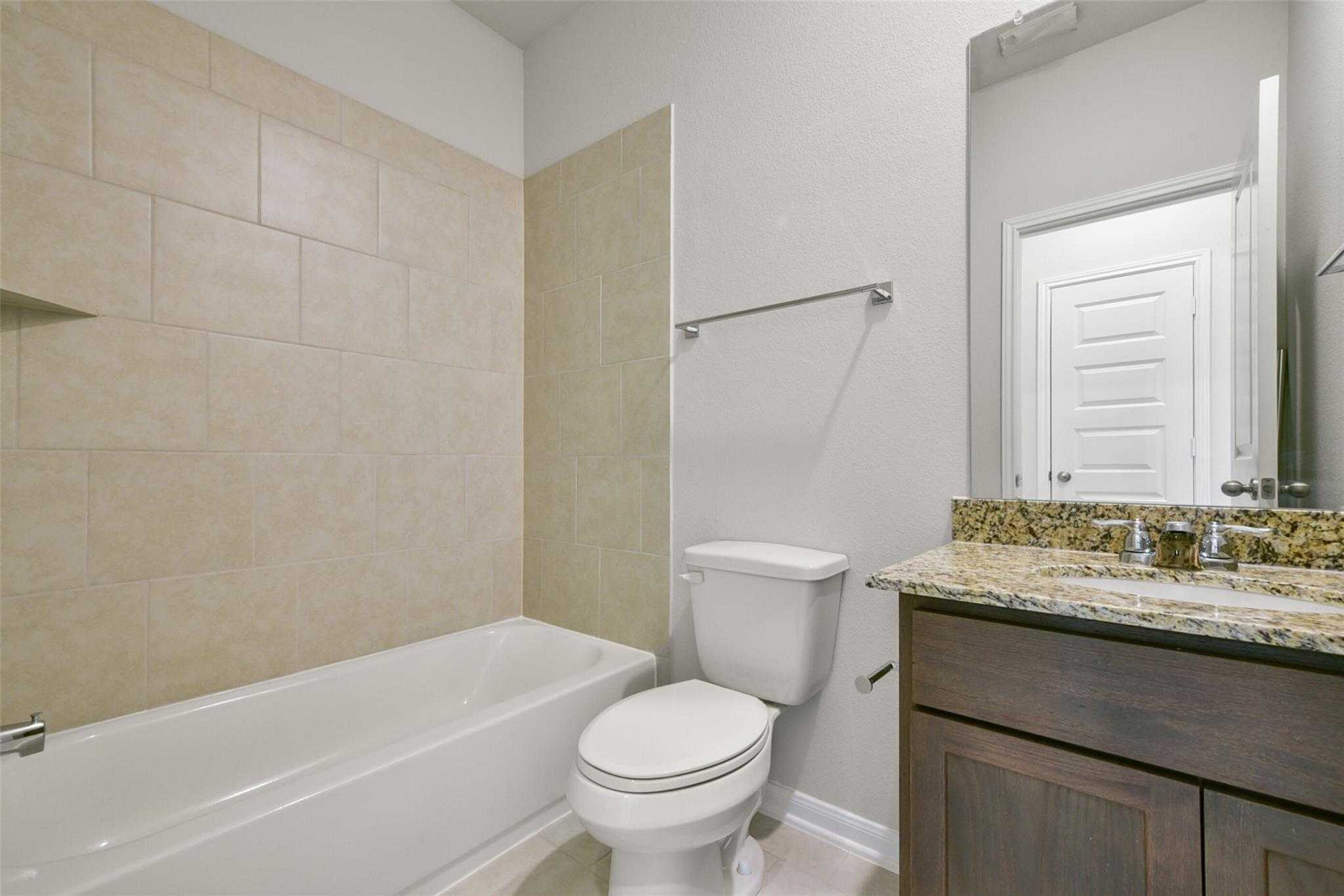 Modern bathroom featuring bathtub, tiled shower, granite vanity, and wood cabinets in Davidson Homes The Sabine E, Dayton Texas