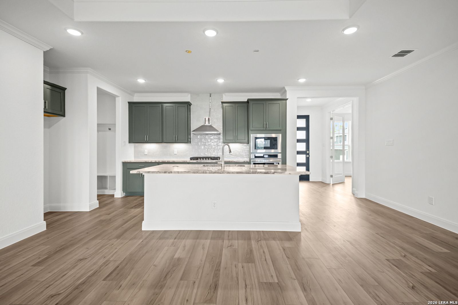 Open-concept kitchen with sage green cabinets, large island, and wood flooring in The Lanier G home, Castroville, Texas.