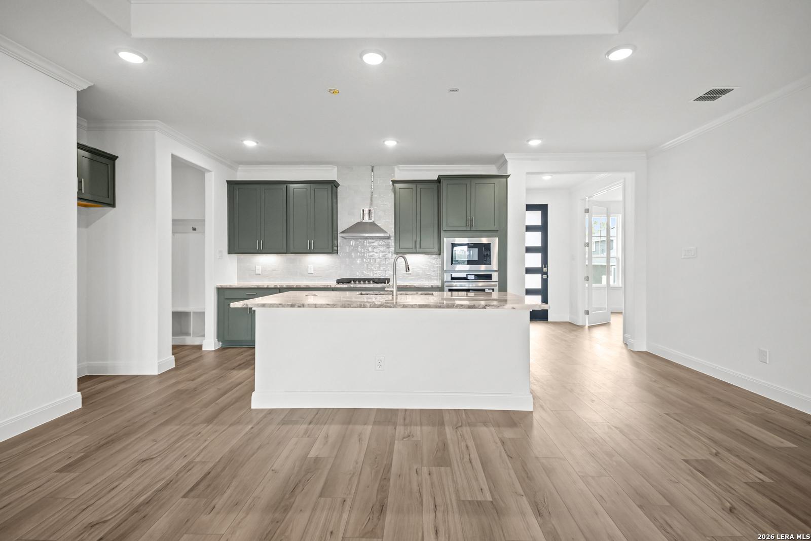 Open-concept kitchen with sage green cabinets, large island, and wood flooring in The Lanier G home, Castroville, Texas.