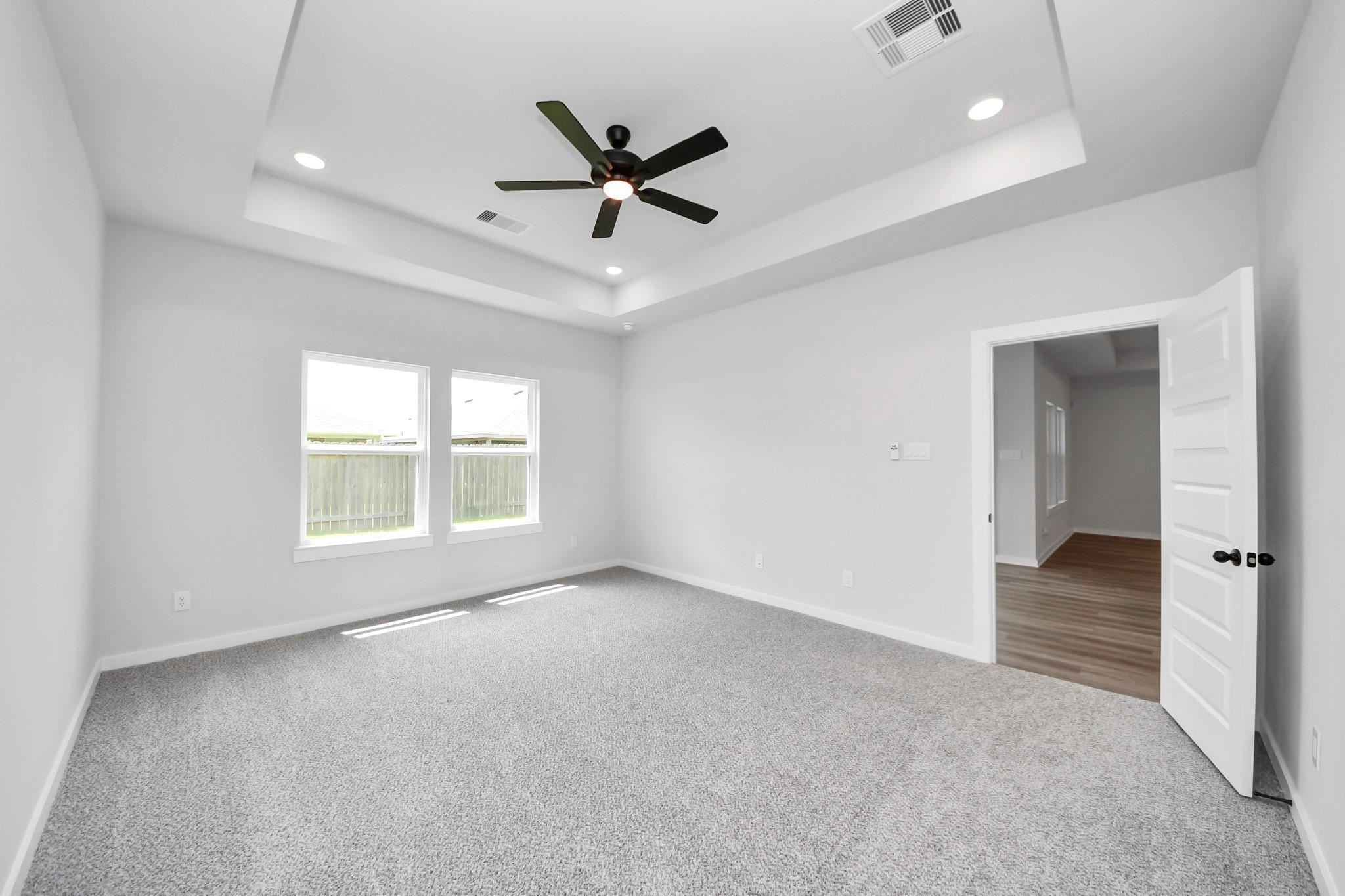 Bright bedroom with tray ceiling and ceiling fan in The Everett C floor plan at River Ranch Meadows in Dayton, Texas.