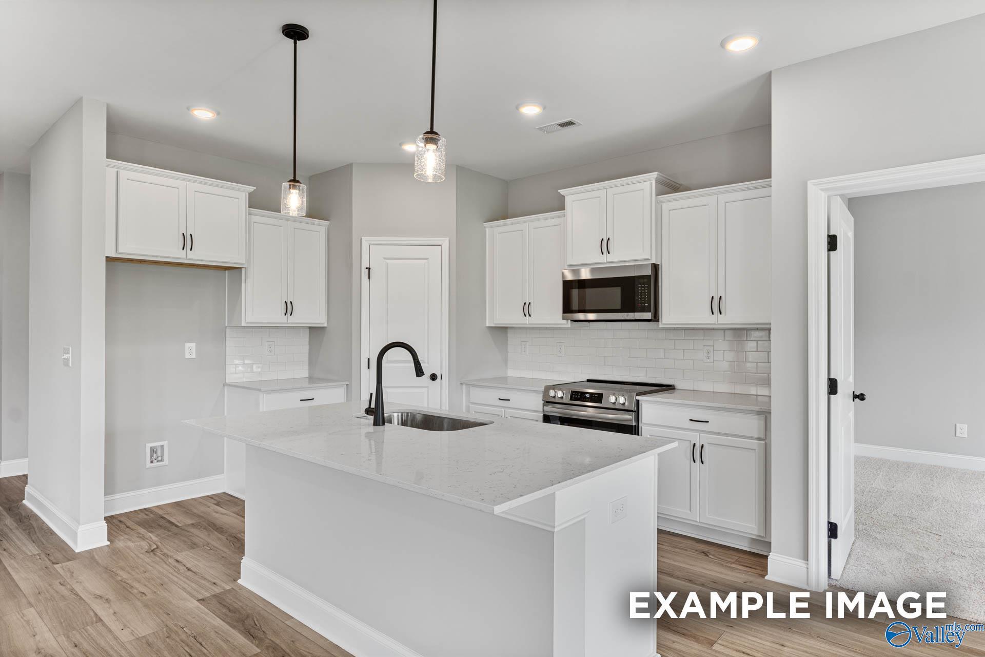 Modern kitchen with white shaker cabinets, quartz island, stainless appliances, subway tile backsplash in Davidson Homes The Franklin C, Athens, AL