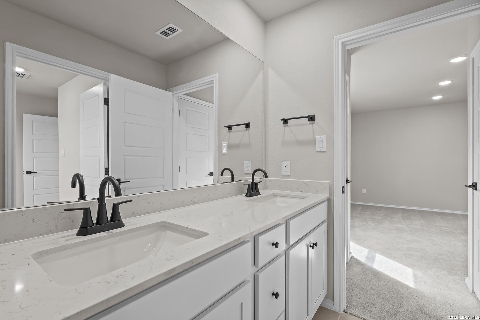 Double vanity bathroom with white cabinets, quartz countertops, and matte black faucets in Davidson Homes The Sequoia C, Royal Crest San Antonio