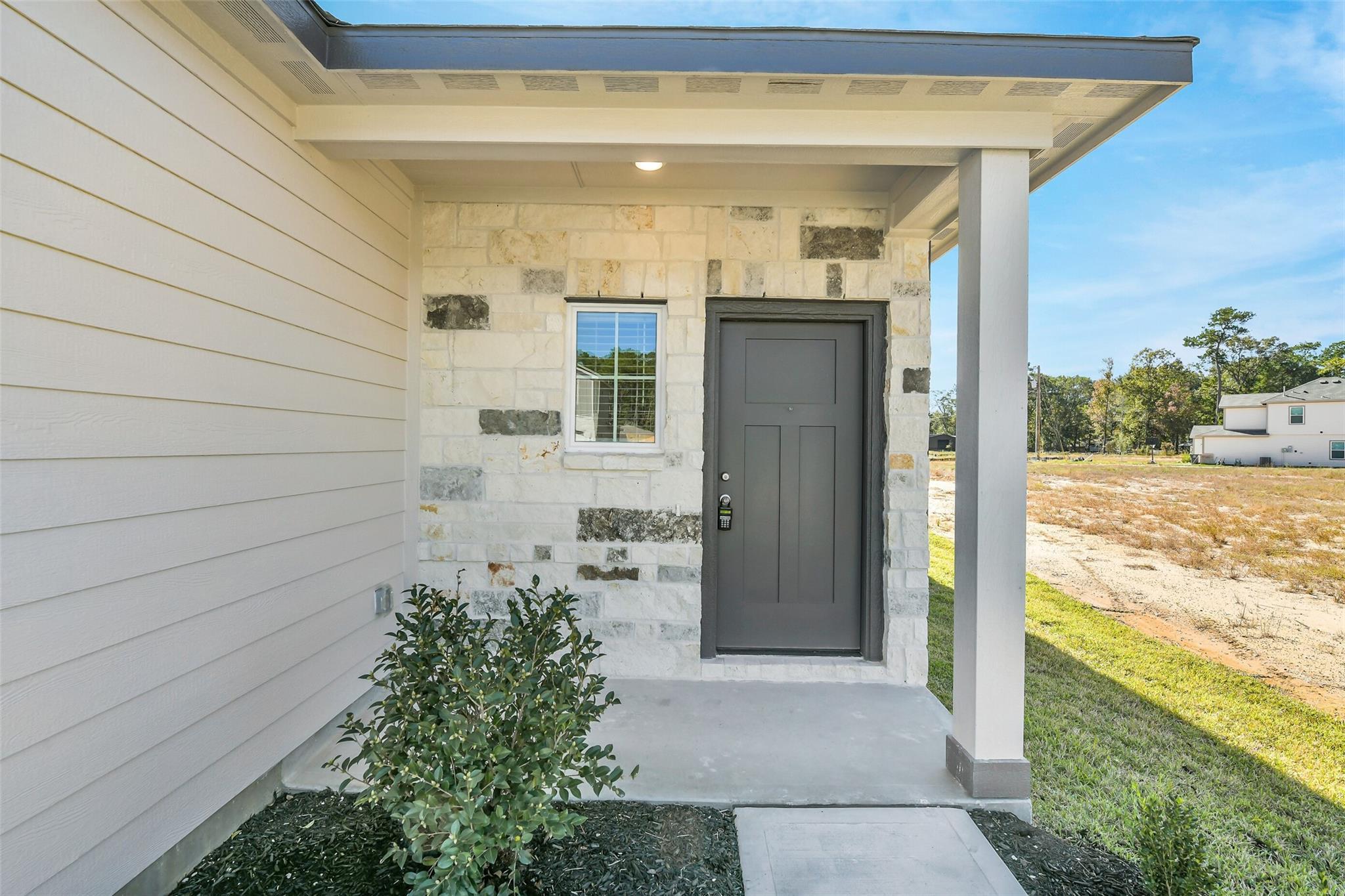 Modern front exterior of Davidson Homes San Marcos E with stone accents, covered porch, and dark door in Liberty Estates, Cleveland, Texas