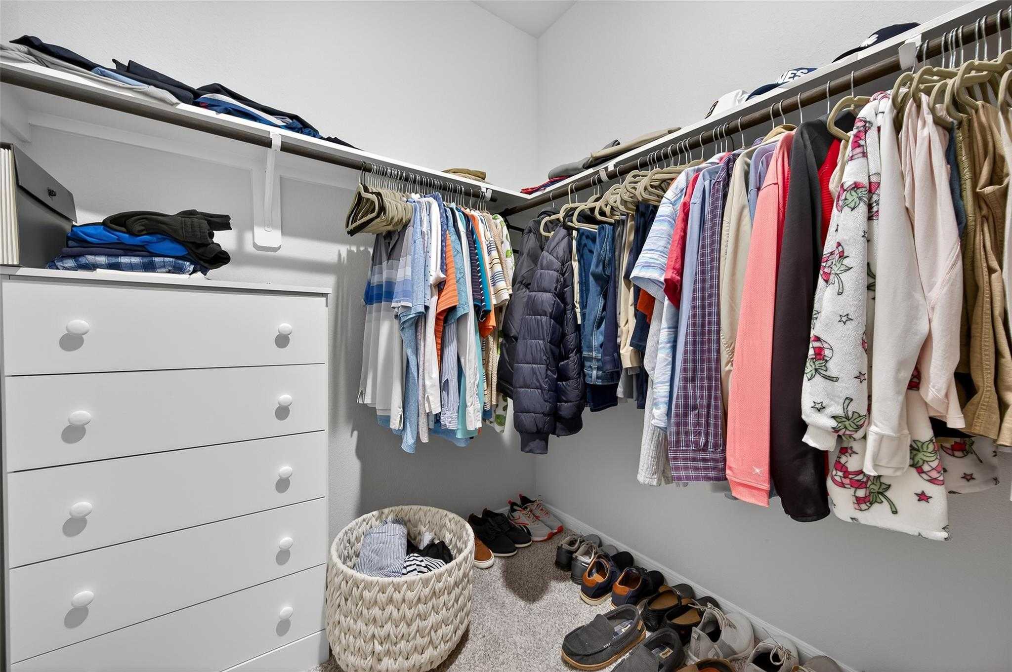 Spacious walk-in closet with organized hanging clothes, white dresser, shoes, and basket in Davidson Homes The Brazos E, Magnolia, Texas