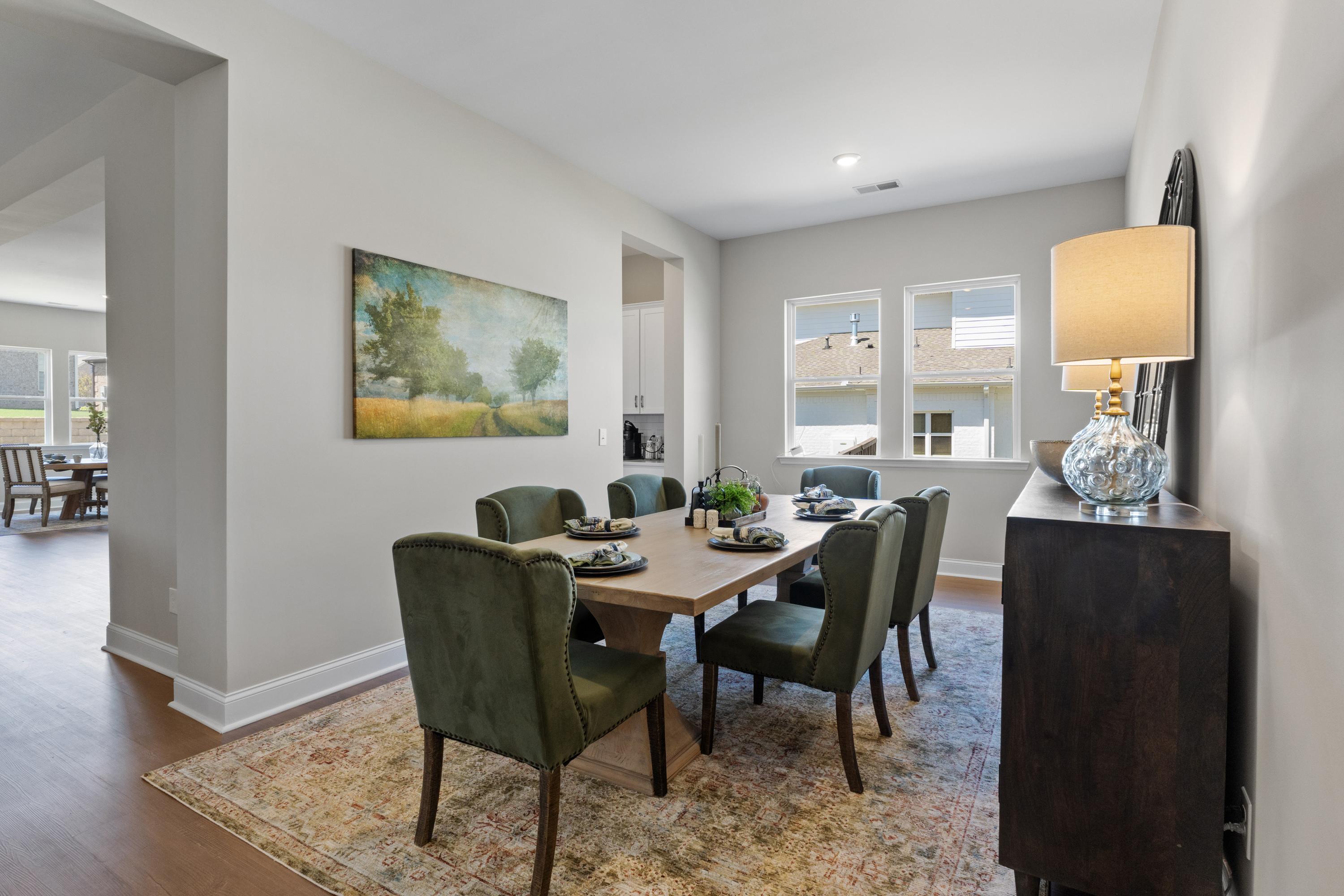 Elegant dining room in The Haven showcasing wood table, green velvet chairs, oriental rug, and landscape artwork