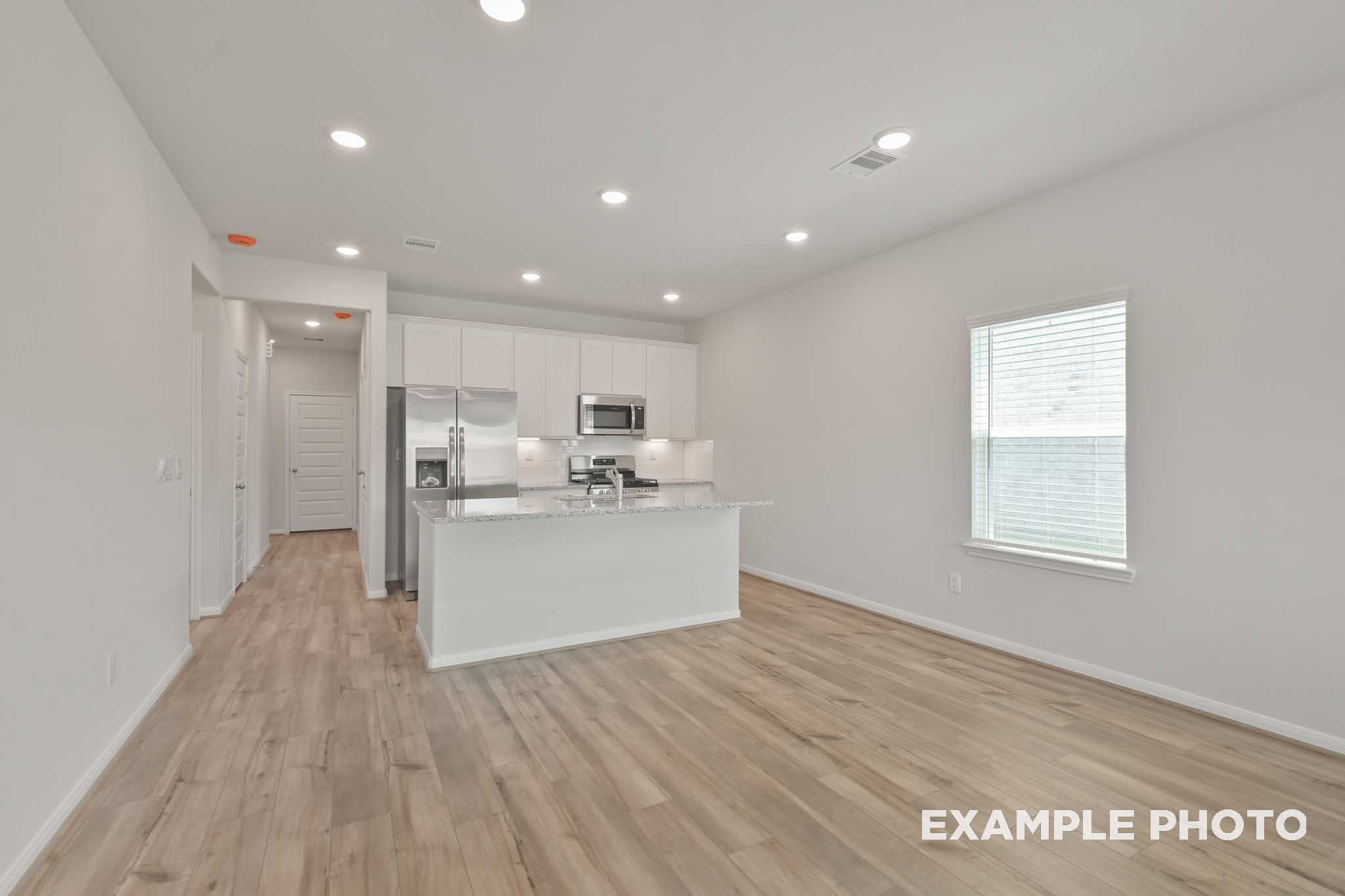 Spacious open-concept kitchen in The Comal with white cabinets, stainless steel appliances, large island, and light wood floors