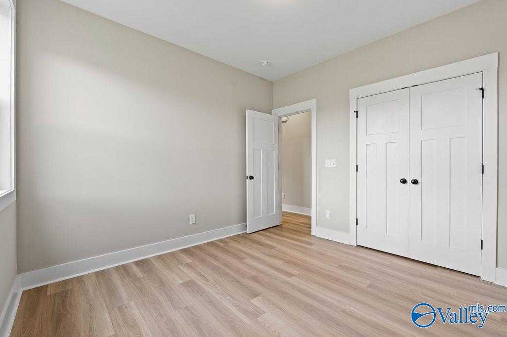 Bright secondary bedroom with beige walls, light hardwood floors, and white double-door closet in Evermore Homes The Oxford, Owens Cross Roads, Alabama