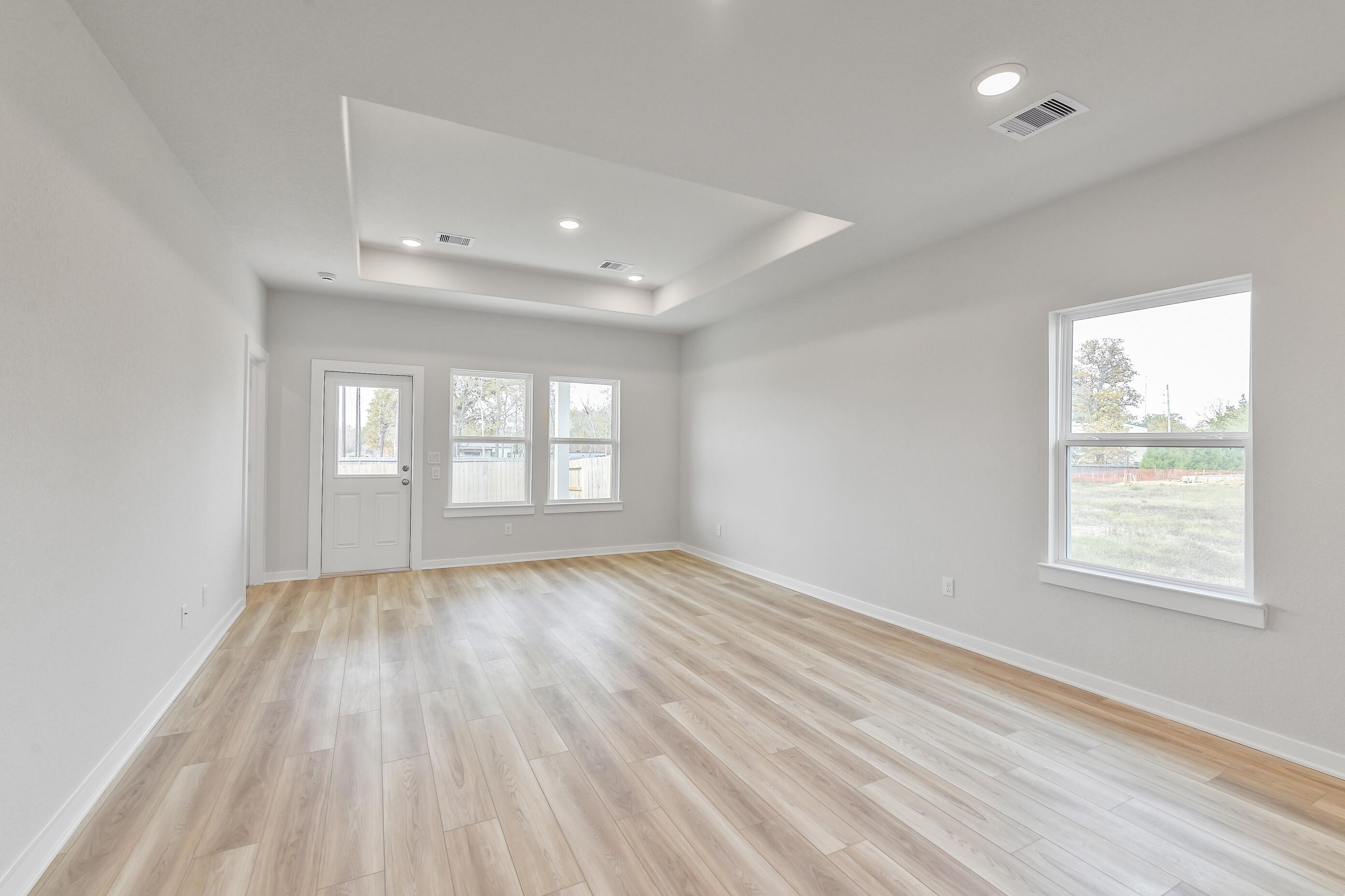 Bright spacious living room with tray ceiling, large windows, and light laminate flooring in Davidson Homes The Colorado G, Magnolia Texas