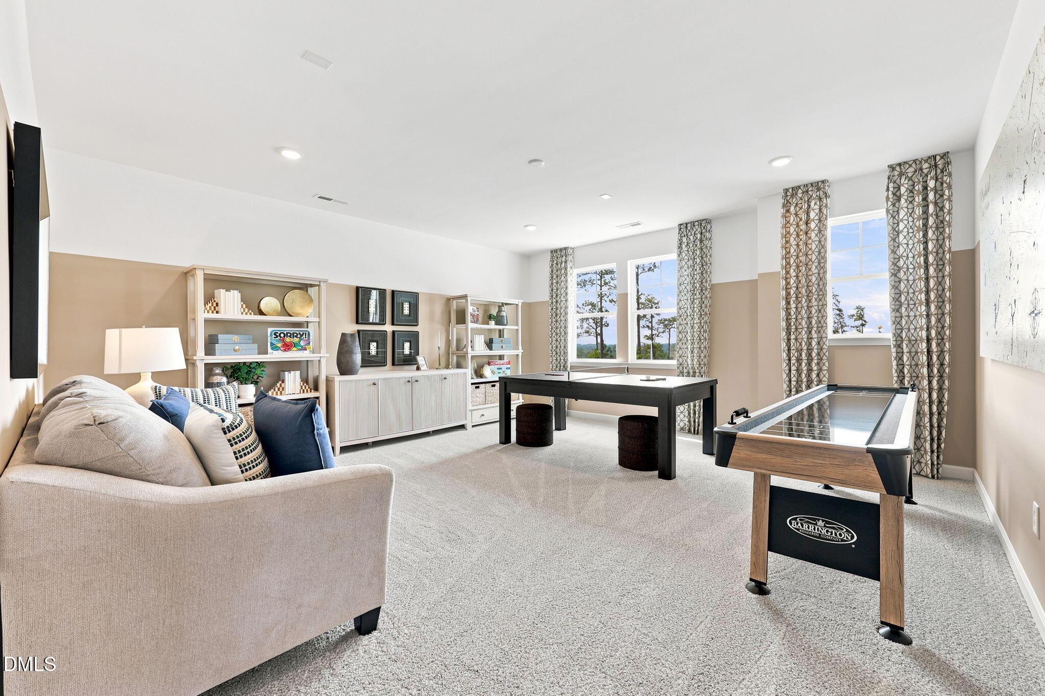 Spacious game room with a lounge area, ping pong table, and shuffleboard in The Beech B home at Addison West, Holly Springs.