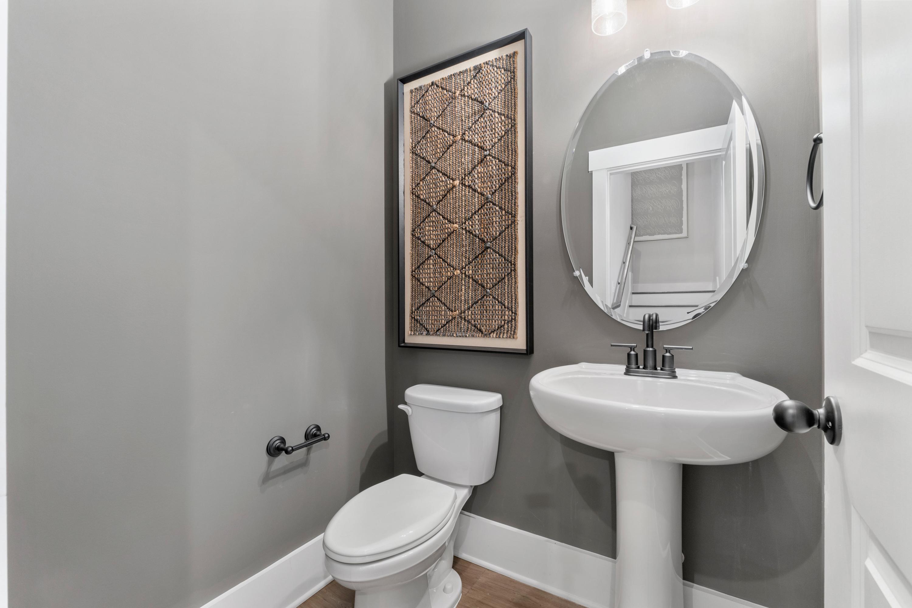 Modern powder room in Little Creek Arab Alabama with gray walls, pedestal sink, round mirror, and woven wall art