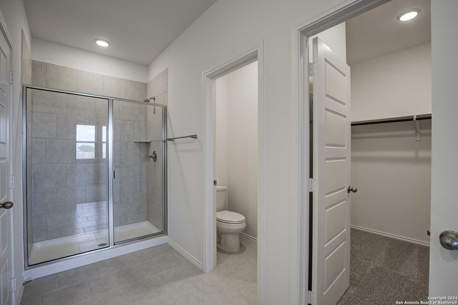 Modern master bathroom featuring frameless glass shower, tiled vanity, toilet, and open walk-in closet in Davidson Homes The Douglas D, Seguin, Texas