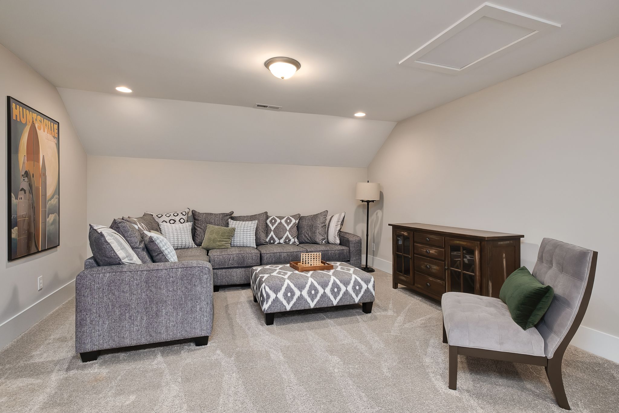 Cozy bonus room in Chimney Creek, Hampton Cove, Alabama with gray L-shaped sectional sofa, sloped ceiling and surfboard art