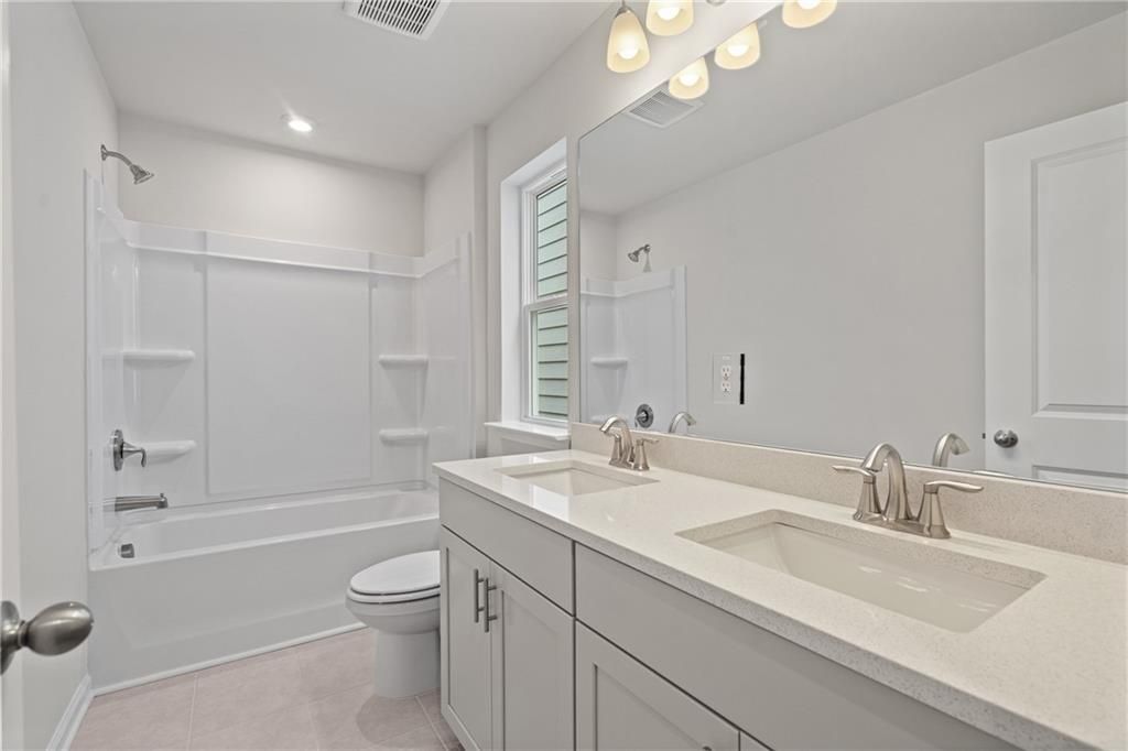 Modern guest bathroom with double quartz vanity, bathtub shower combo, and white cabinetry in The Marion B home, Kennesaw, GA