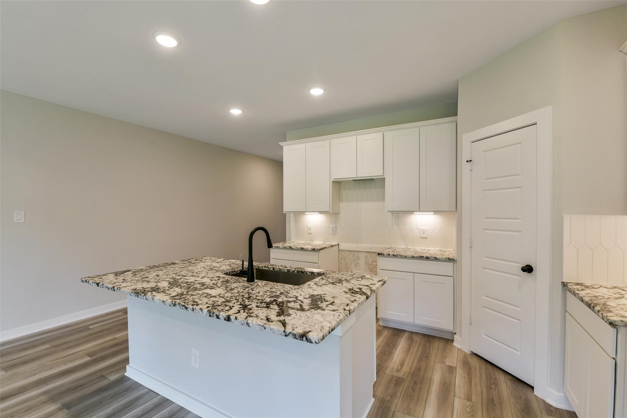 Modern white kitchen with granite island, black faucet, and open layout in The Daphne H by Davidson Homes, Crosby, TX