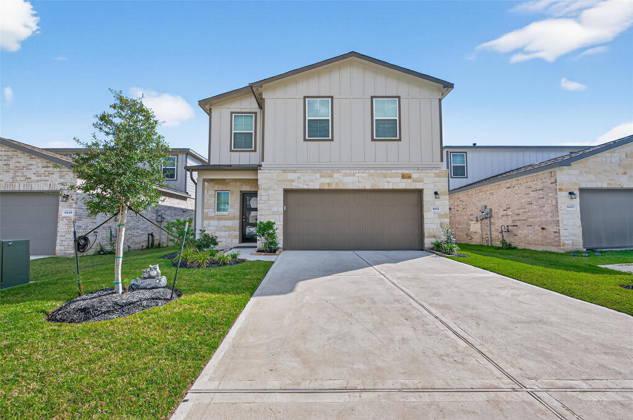 Modern two-story beige home with two-car garage, driveway, and landscaped lawn in Lakes at Black Oak, Magnolia, Texas
