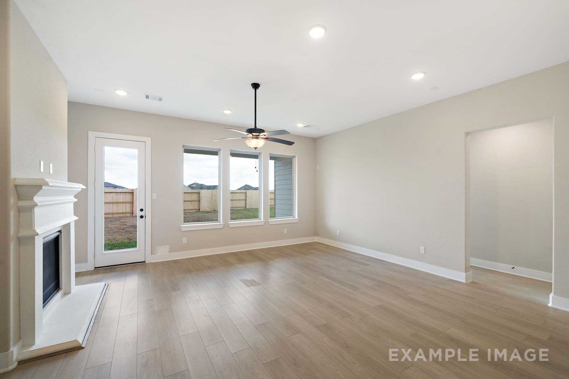 Spacious living room in The Elizabeth A showcasing white fireplace, large windows, ceiling fan, and light hardwood floors