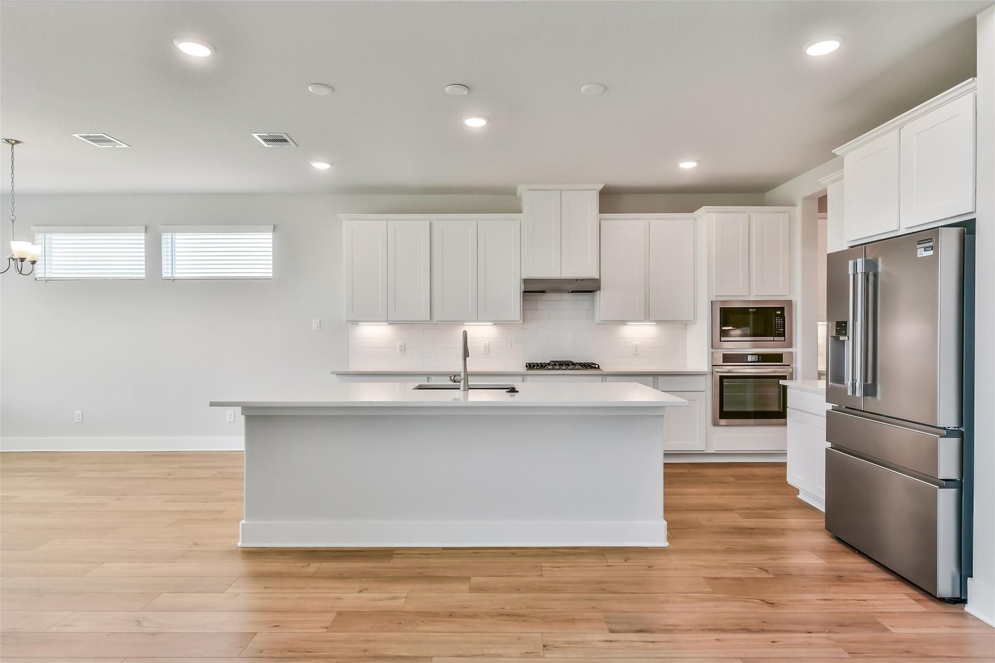 Bright modern kitchen with white shaker cabinets, large quartz island, stainless steel fridge and double oven in Davidson Homes Victoria A, Lago Mar