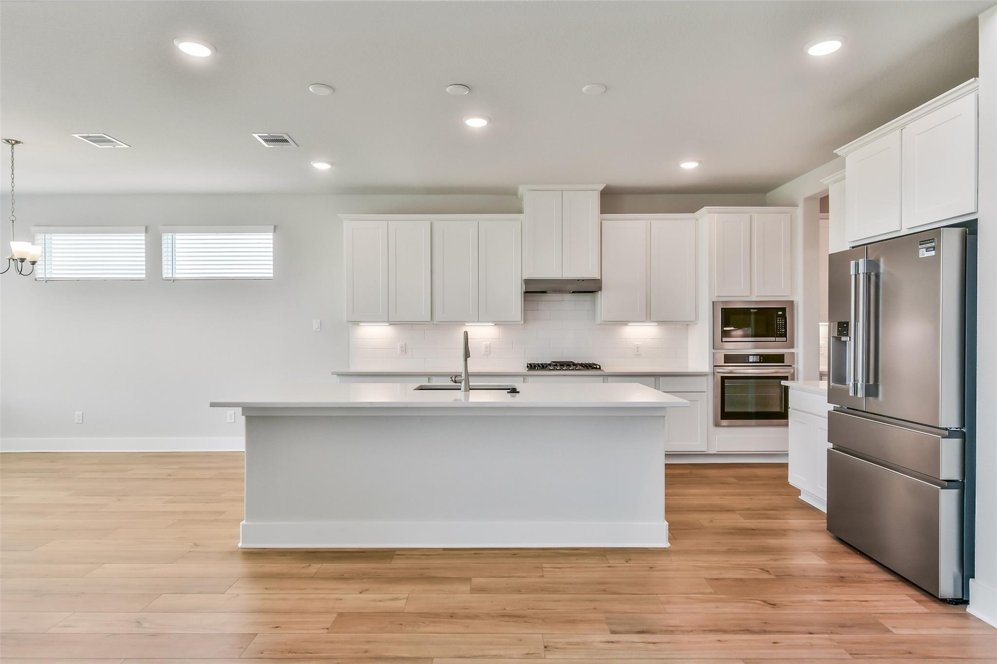 Bright modern kitchen with white shaker cabinets, large quartz island, stainless steel fridge and double oven in Davidson Homes Victoria A, Lago Mar