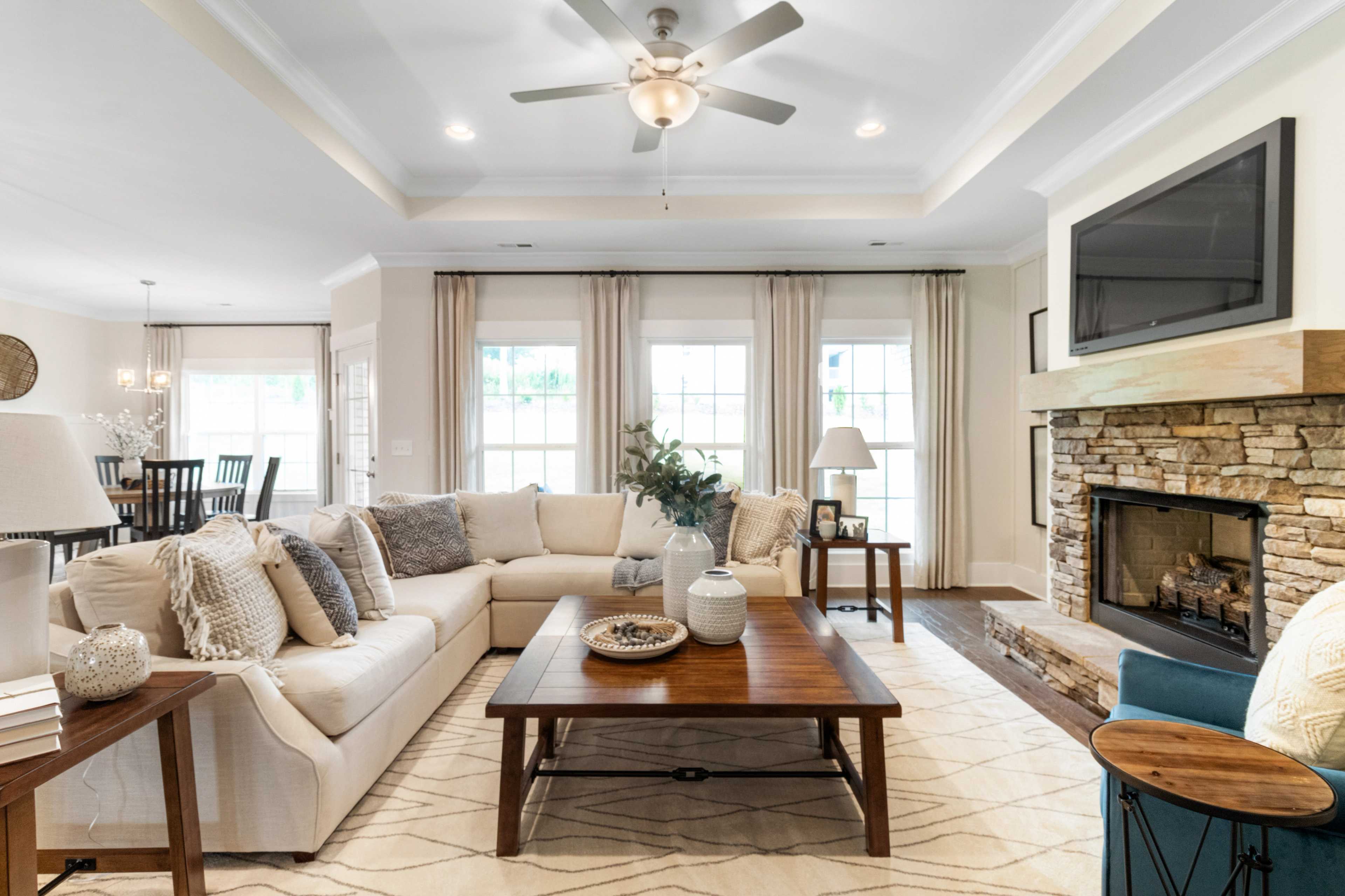Cozy open-concept living room in Noble Ridge Cullman Alabama with stone fireplace beige L-shaped sofa ceiling fan and large windows