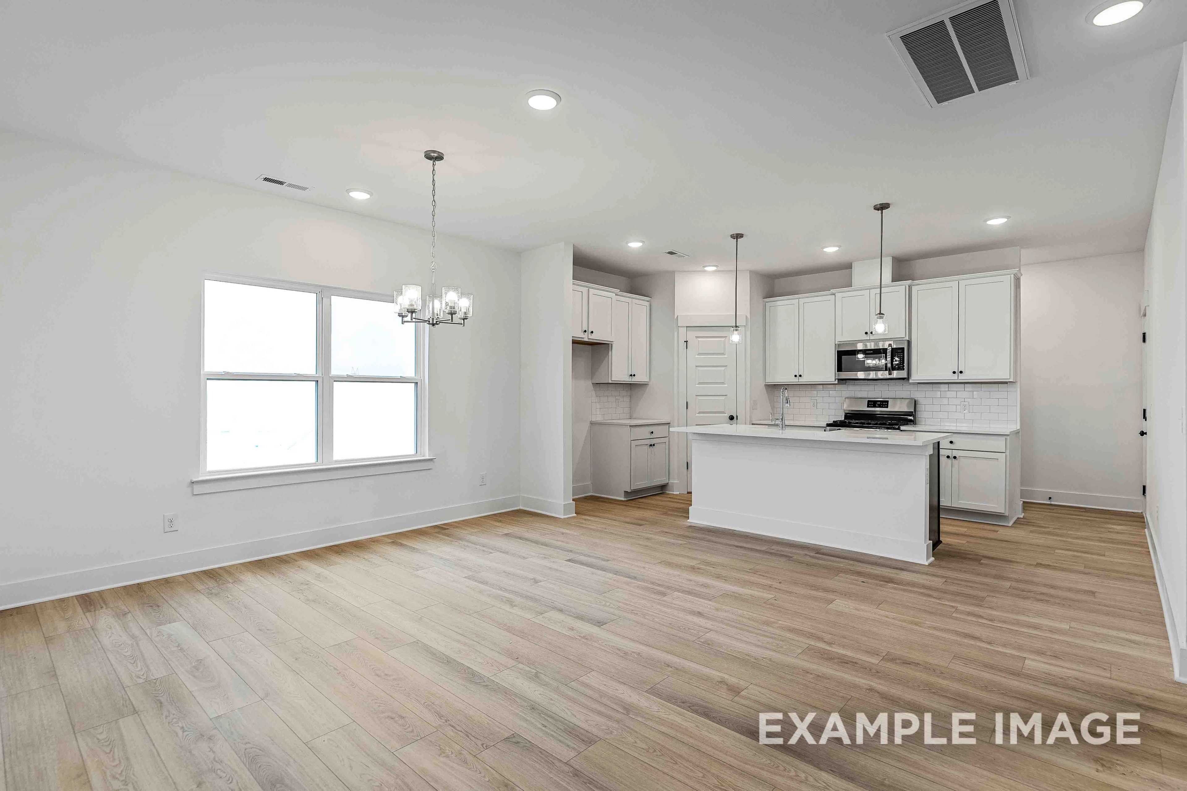 Spacious open-concept kitchen and dining in The Charleston C with white cabinets, large island, hardwood floors