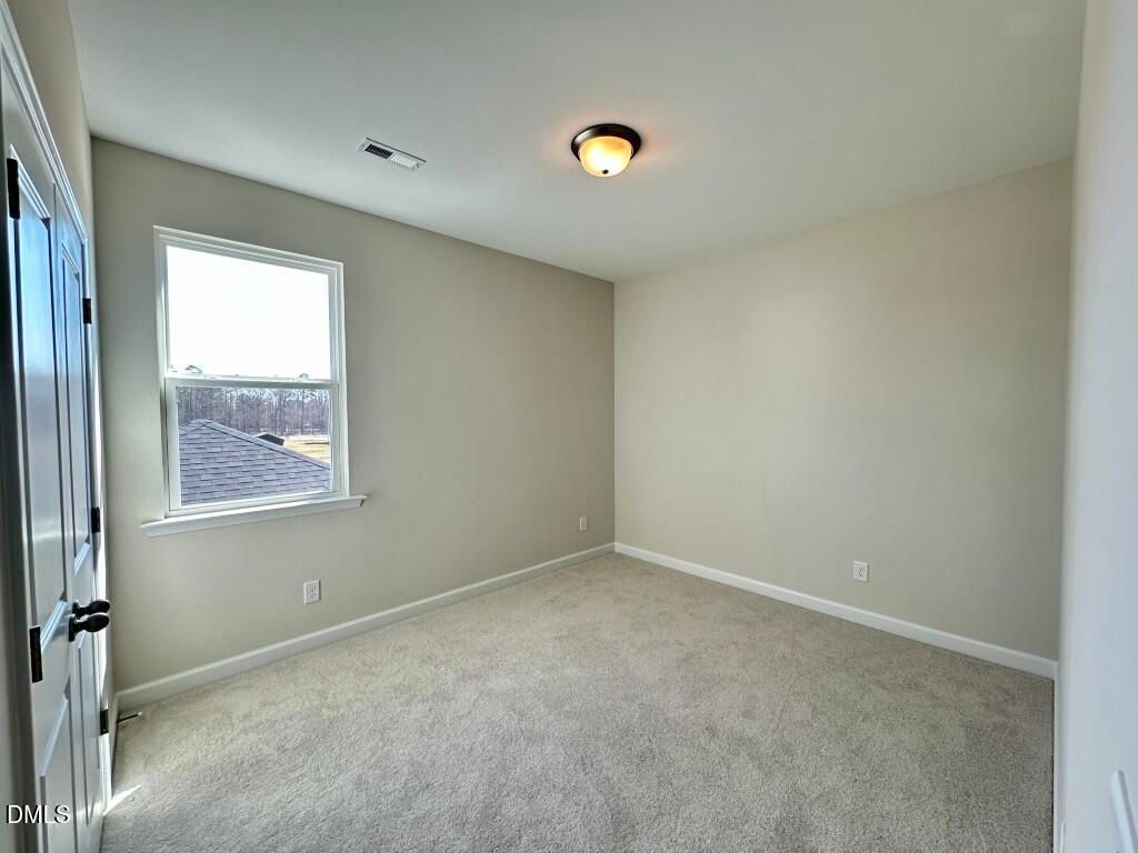 Bright empty bedroom with beige walls, carpet floor, large window, and closet doors in Davidson Homes The Burke, Knightdale, NC