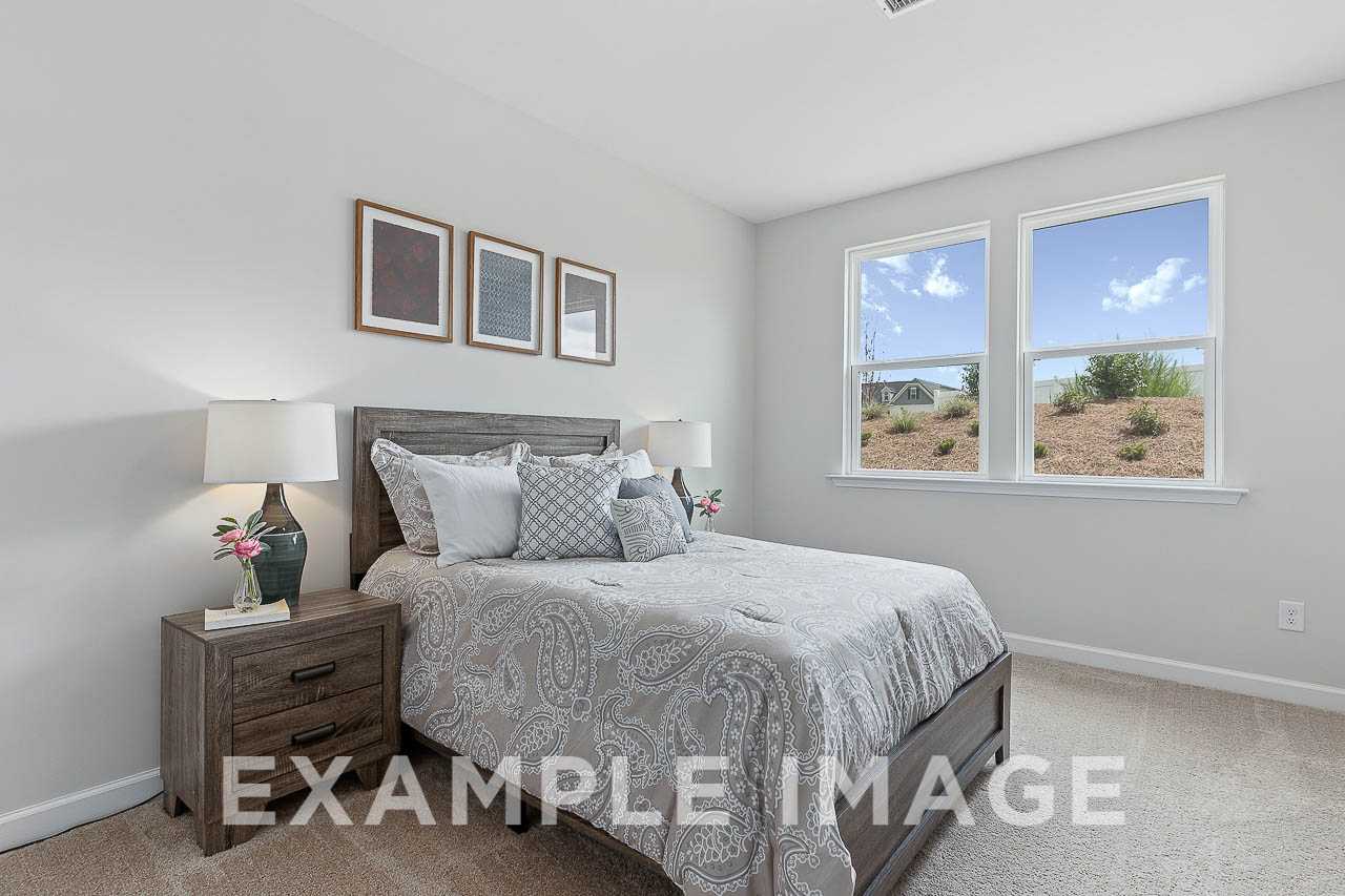 Spacious master suite in The Willow C featuring gray king bed, wooden nightstands, lamps, and large windows with landscape view