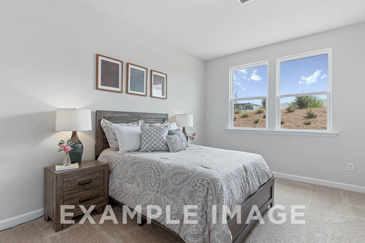Spacious master suite in The Willow C featuring gray king bed, wooden nightstands, lamps, and large windows with landscape view