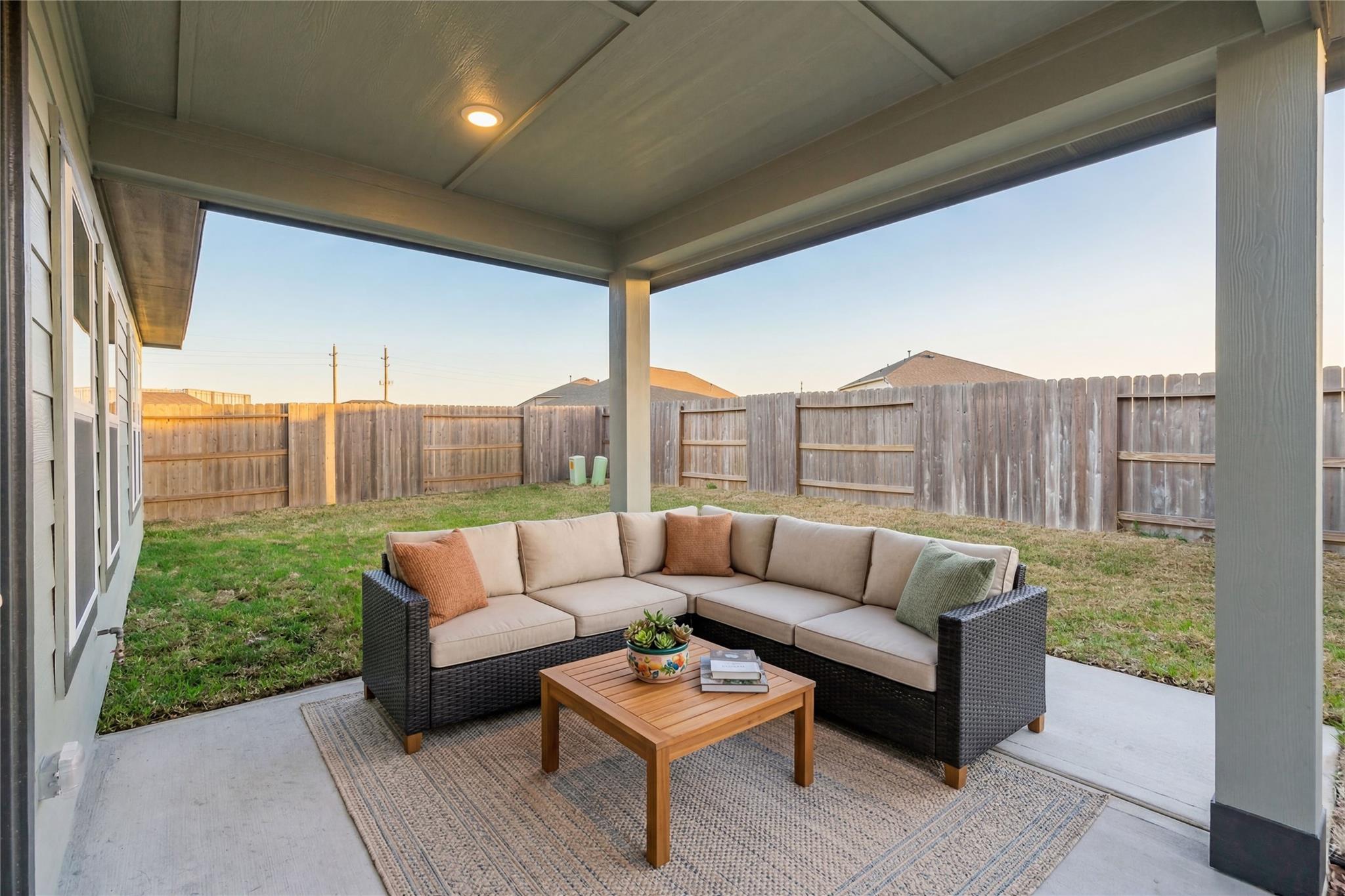 Cozy covered back patio with L-shaped wicker sofa, wooden coffee table, plants and rug in Davidson Homes The Luna L, Sunterra, Katy, Texas