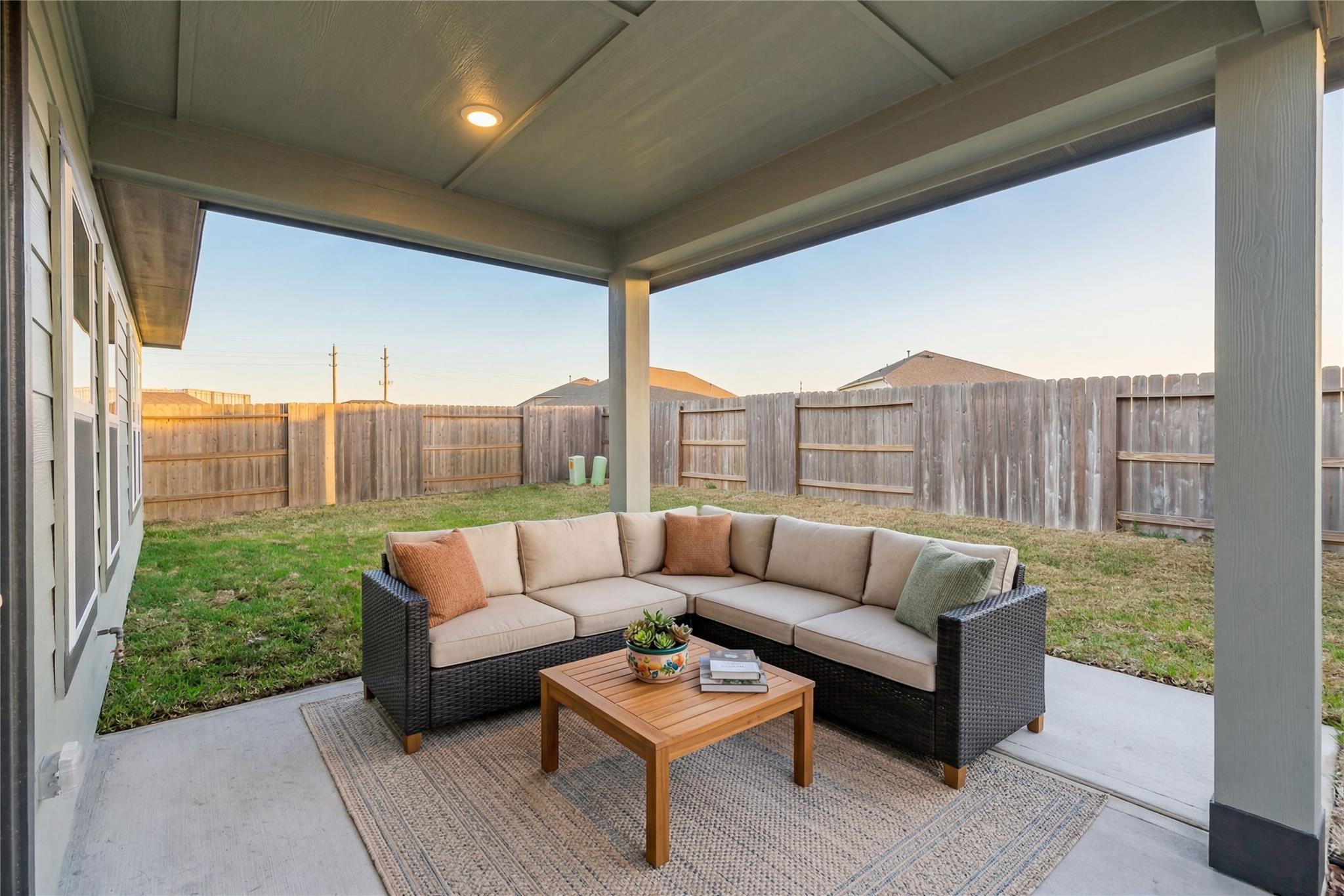 Cozy covered back patio with L-shaped wicker sofa, wooden coffee table, plants and rug in Davidson Homes The Luna L, Sunterra, Katy, Texas