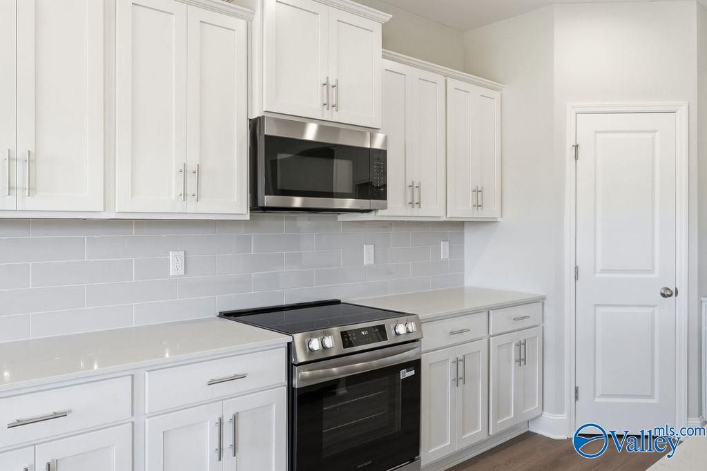 Modern white kitchen with quartz counters, stainless steel range and microwave, subway tile backsplash in The Harrison, Hartselle, AL