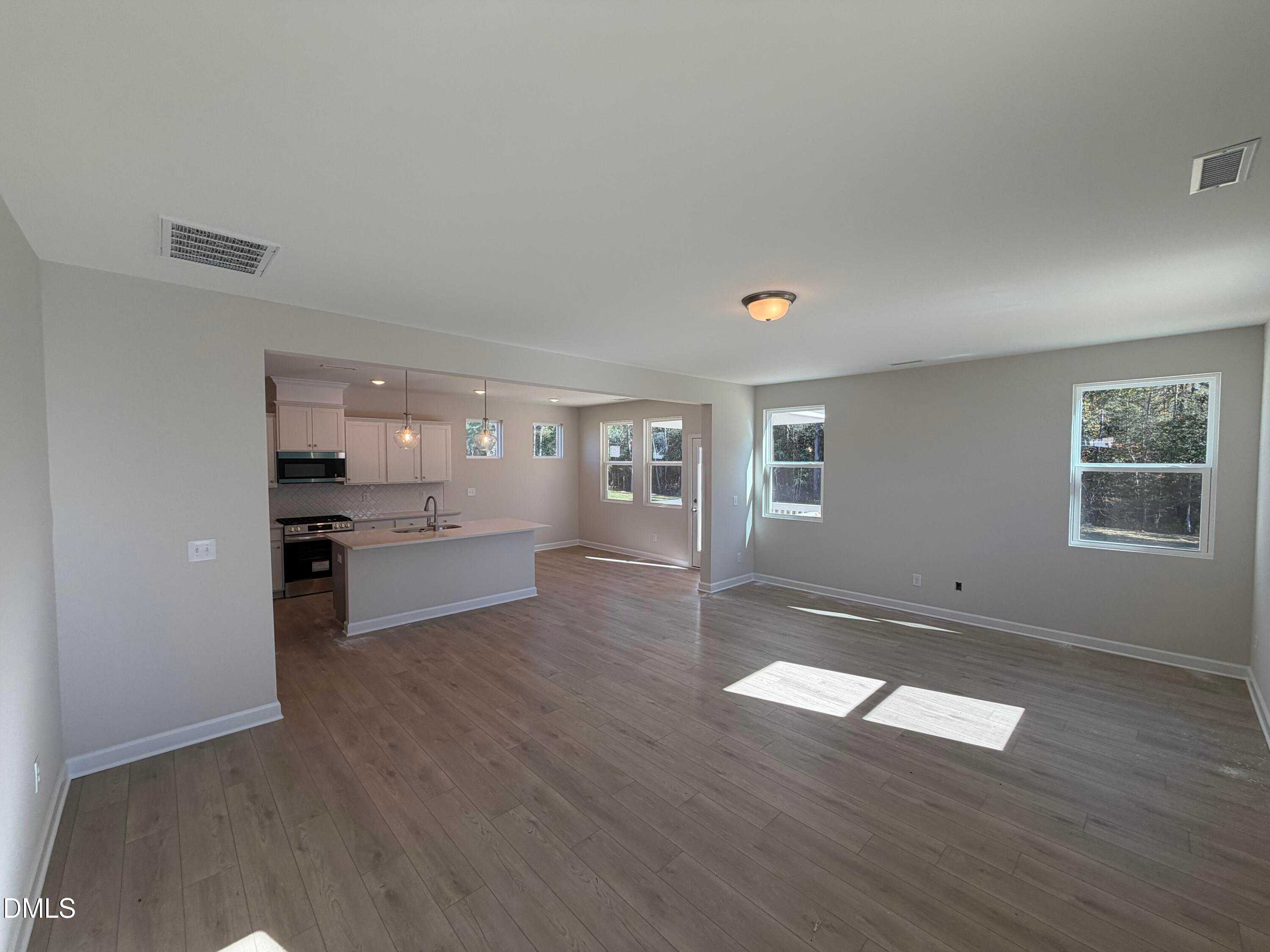 Open-concept kitchen with white cabinets, island sink, and stainless appliances flowing into sunny living room in The Gavin C, Lillington, NC