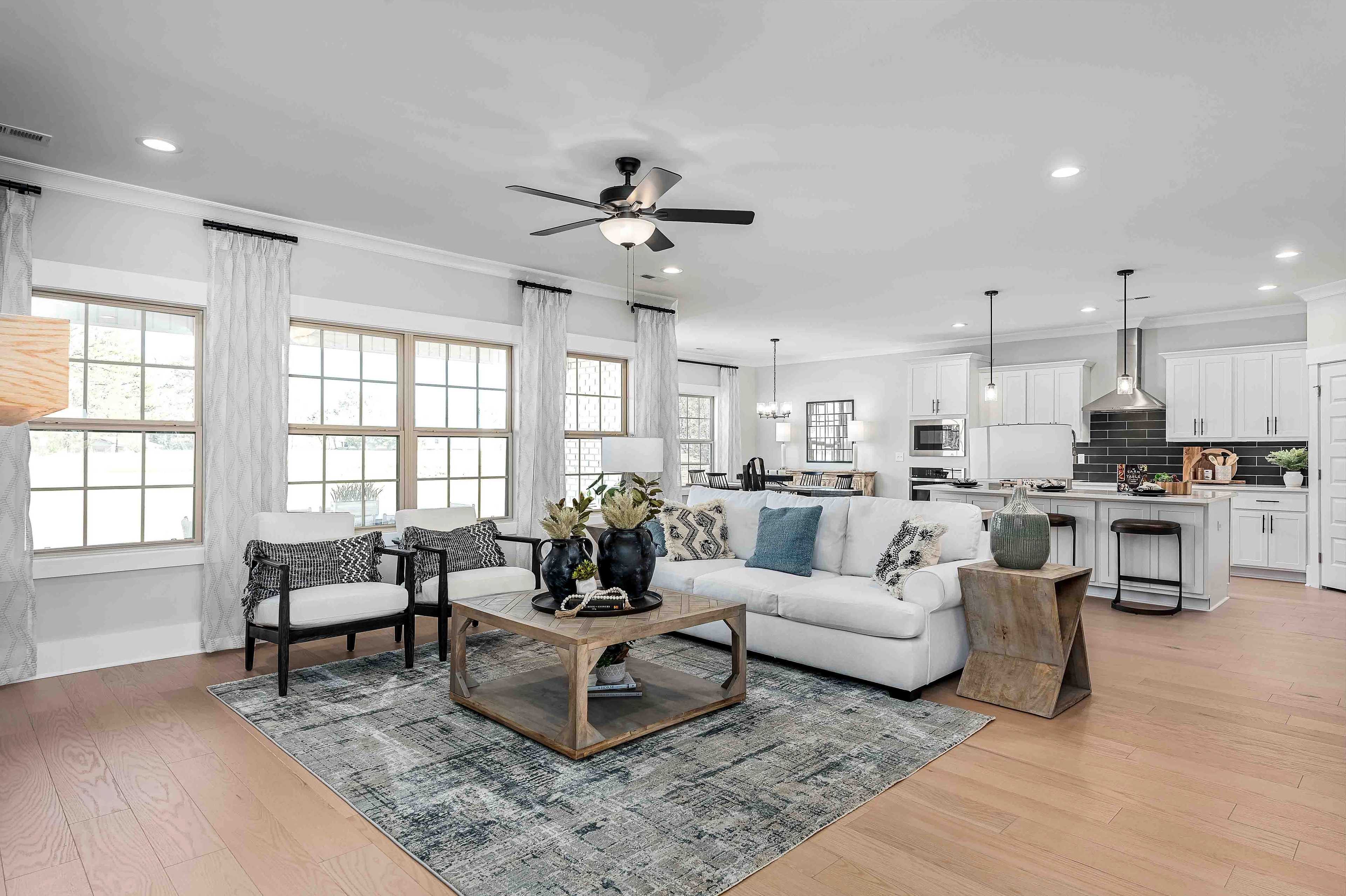 Open-concept living room and kitchen in Cain Park Hartselle AL home with white cabinets, hardwood floors, large windows and ceiling fan