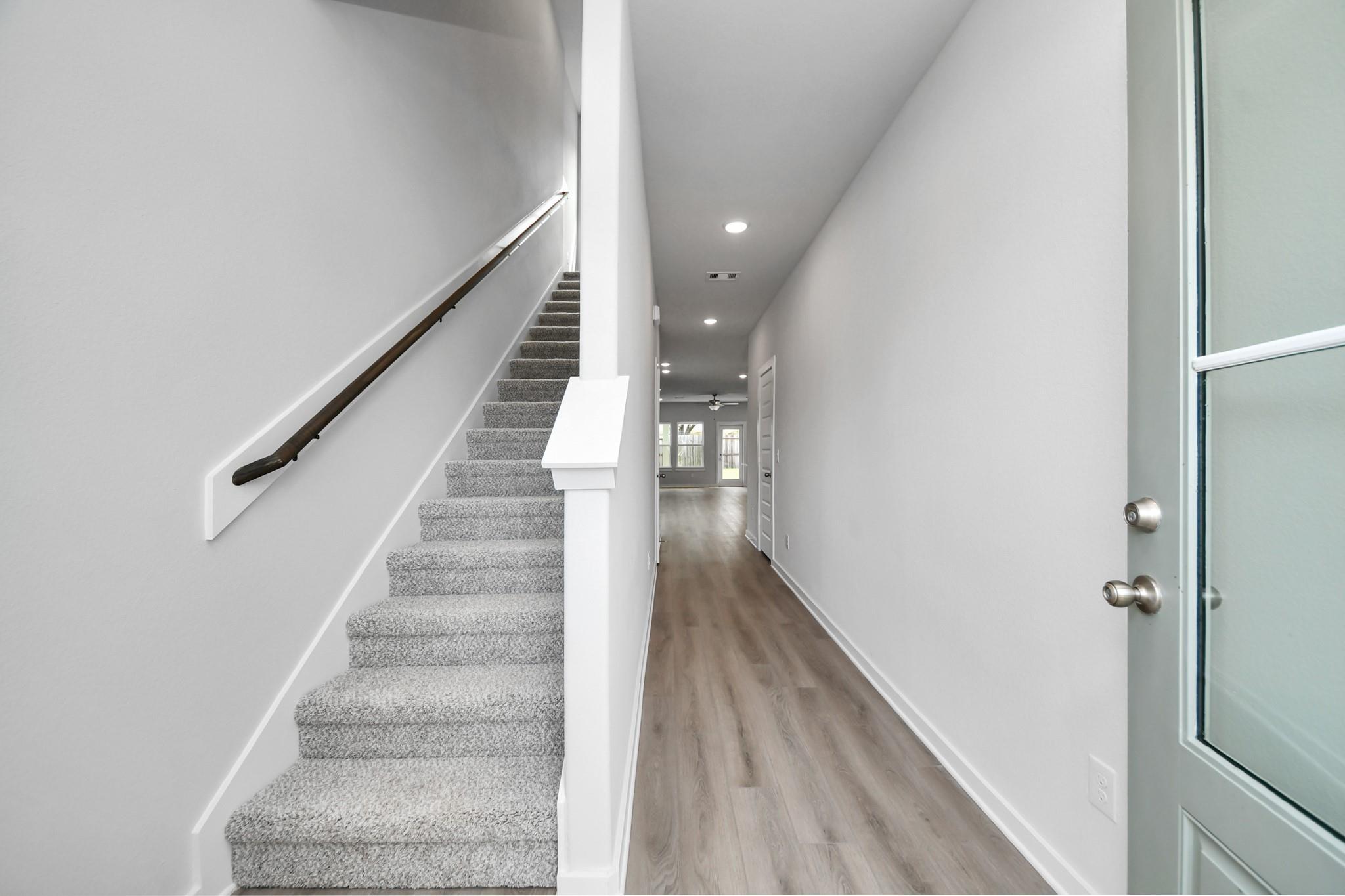 Bright entry foyer with carpeted staircase and wood-look flooring in Davidson Homes' The Blanco E, Windmill Estates, Magnolia, TX