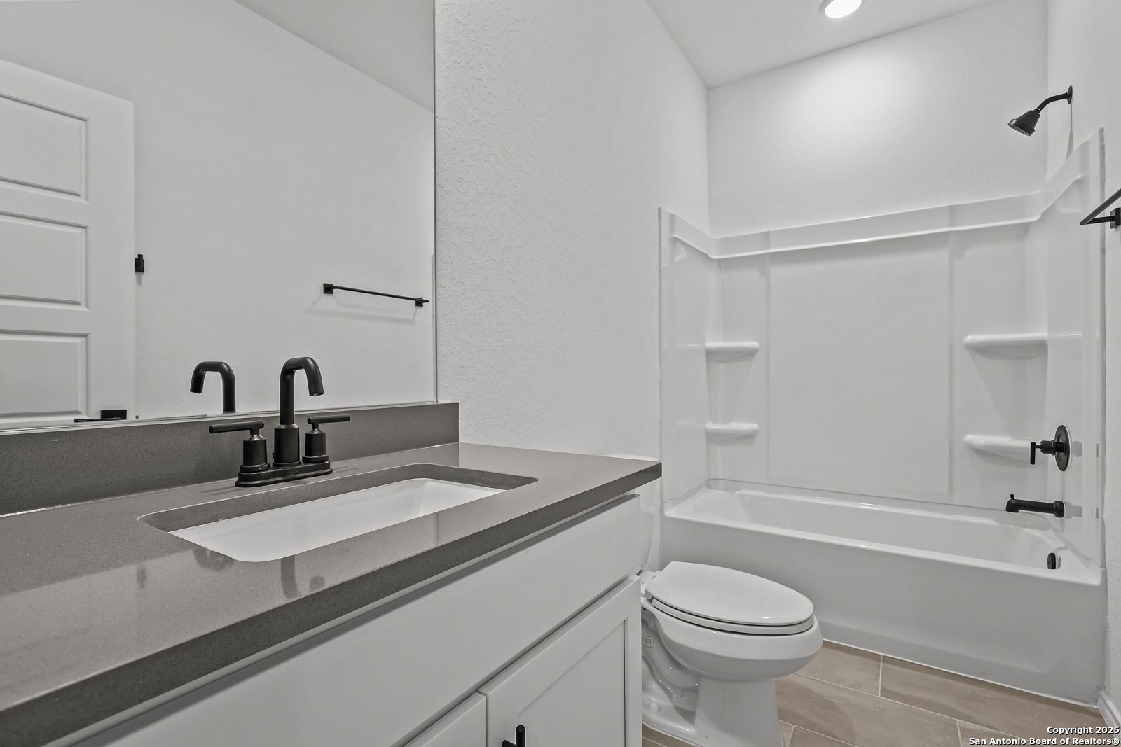 Modern guest bathroom with gray quartz vanity, white cabinetry, deep tub, shower, and black fixtures in The Daphne J, Converse TX