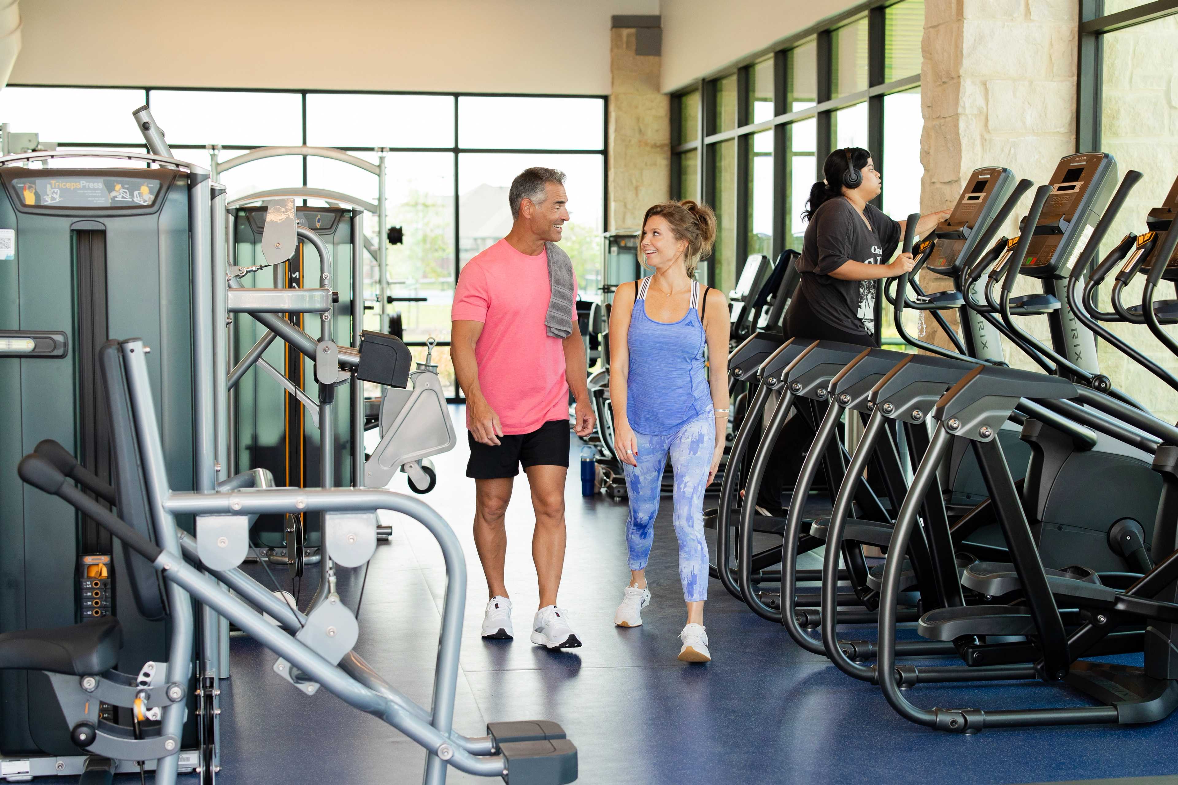 Modern fitness center at Sunterra in Katy Texas with treadmills ellipticals weights and active couple walking