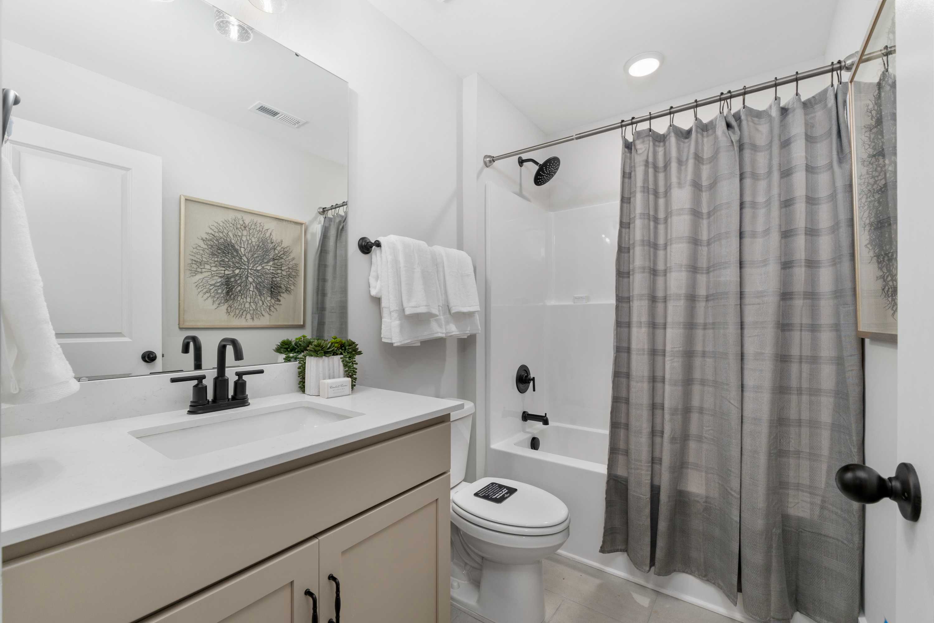 Modern bathroom at Kendall Farms in Toney, Alabama with white subway tile shower, gray plaid curtain, soaking tub, and beige vanity