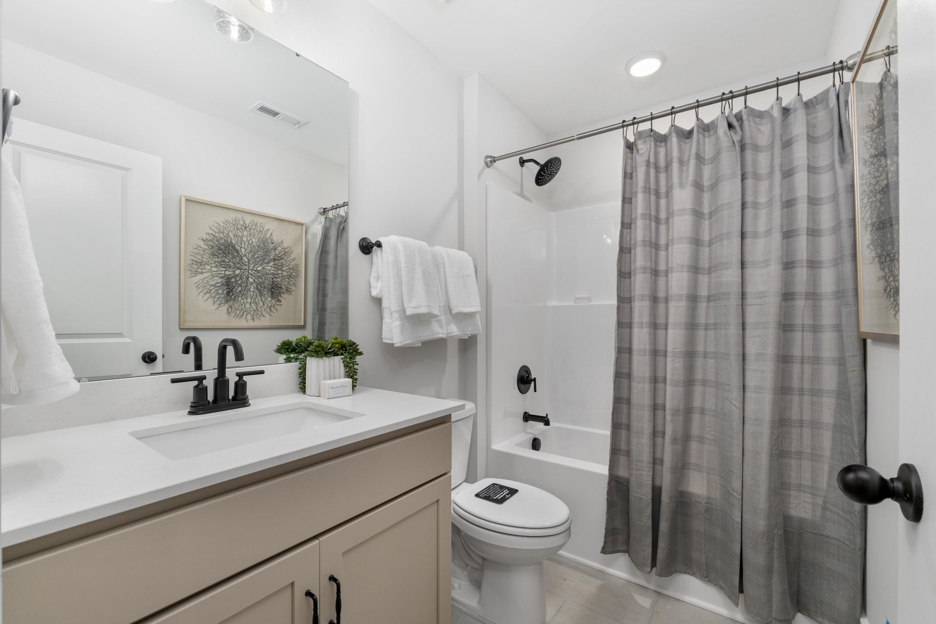 Modern bathroom at Kendall Farms in Toney, Alabama with white subway tile shower, gray plaid curtain, soaking tub, and beige vanity