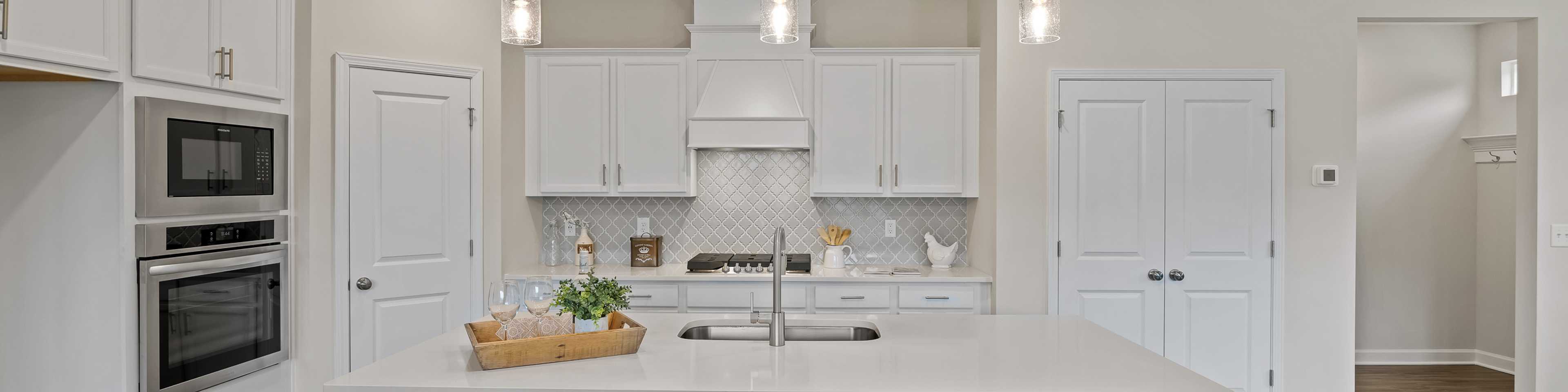 Spacious white kitchen in Gregory Village Lillington NC with central island, bar stools, pendant lights and hardwood floors by Davidson Homes