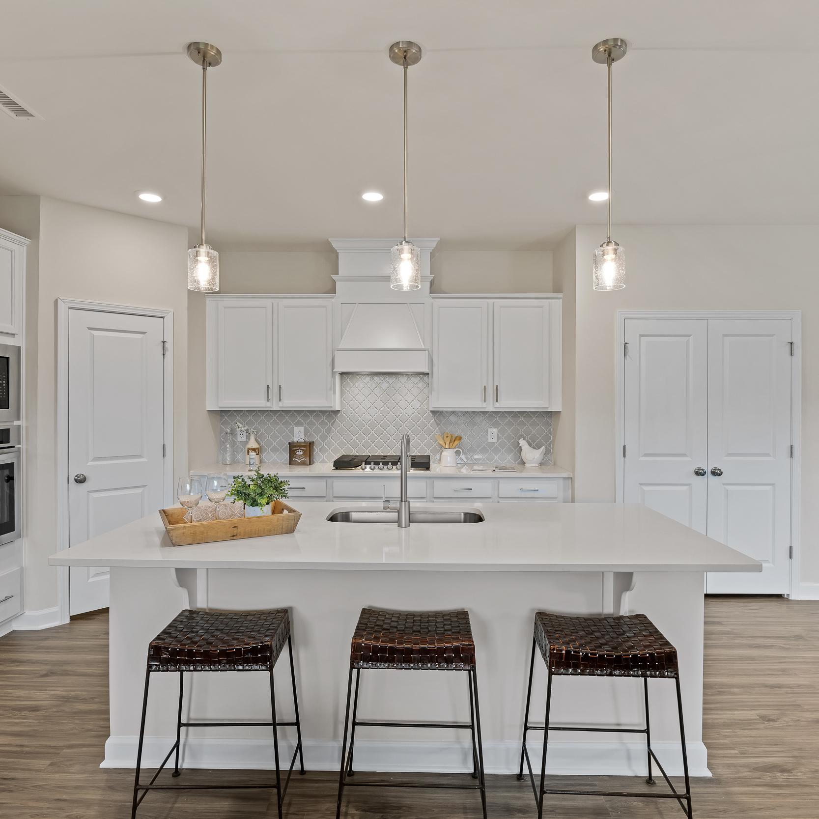 Spacious white kitchen in Gregory Village Lillington NC with central island, bar stools, pendant lights and hardwood floors by Davidson Homes