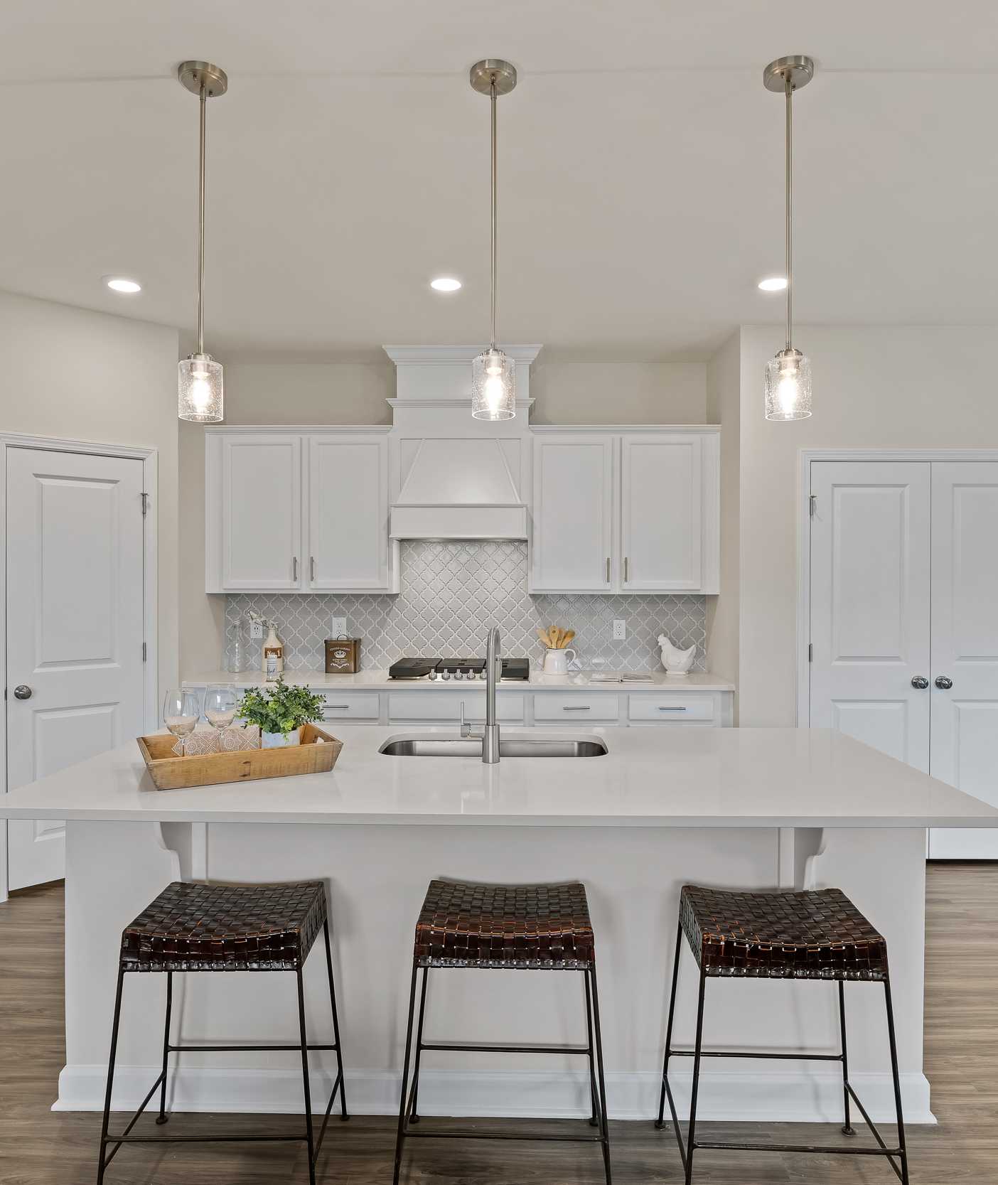 Spacious white kitchen in Gregory Village Lillington NC with central island, bar stools, pendant lights and hardwood floors by Davidson Homes
