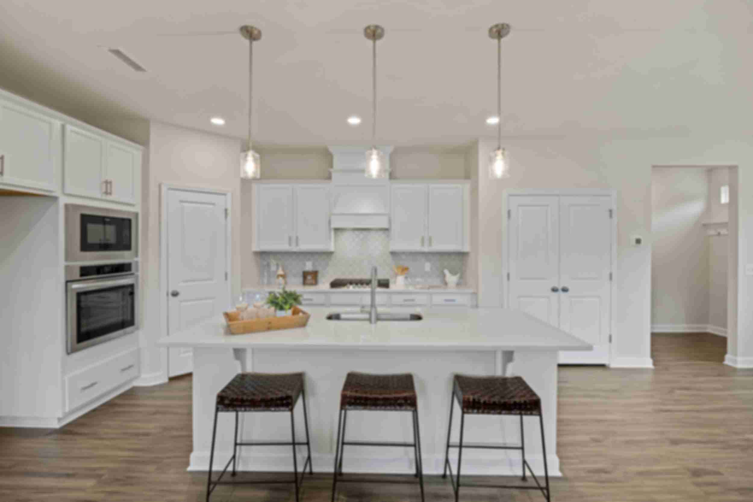 Spacious white kitchen in Gregory Village Lillington NC with central island, bar stools, pendant lights and hardwood floors by Davidson Homes
