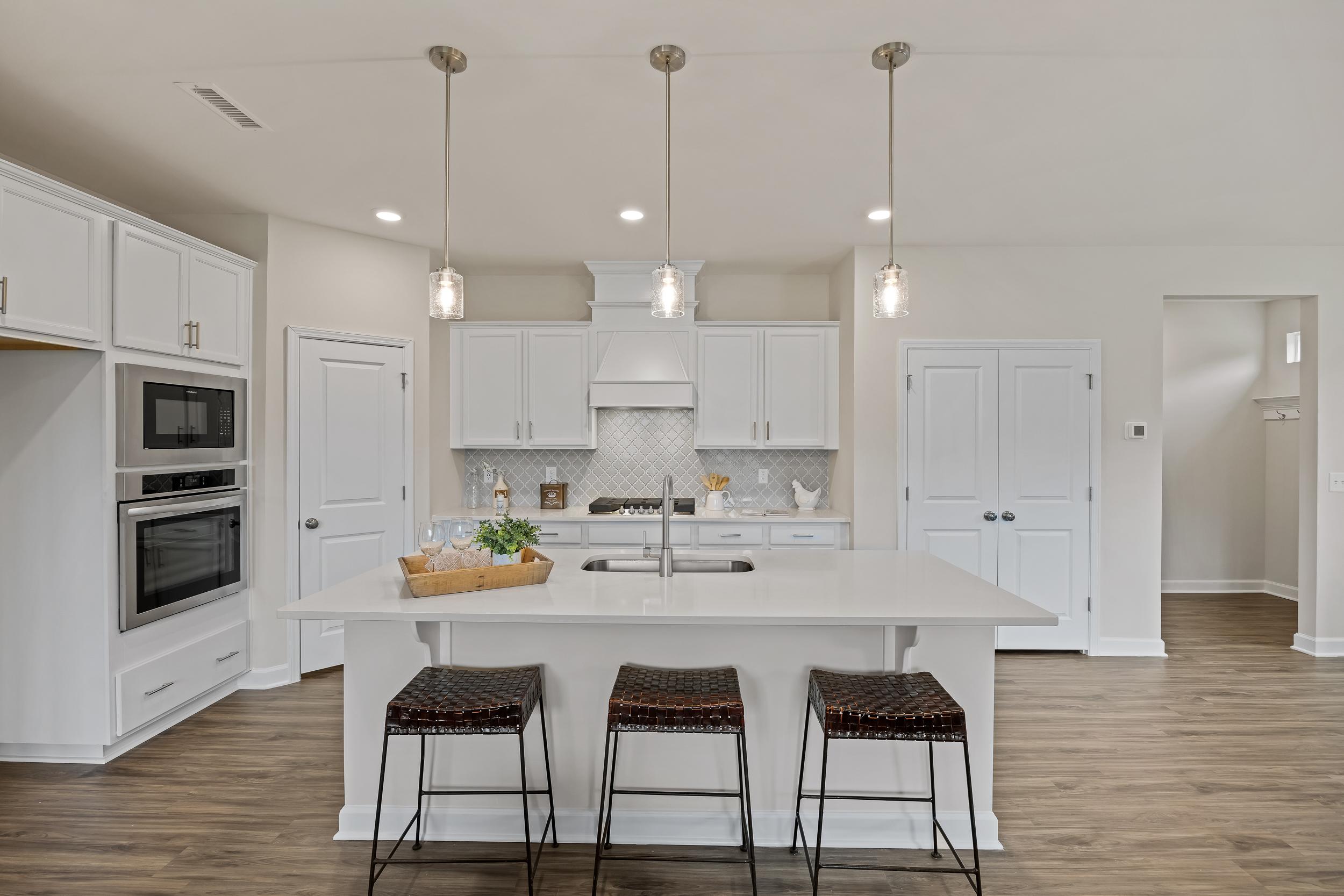 Bright white kitchen with large island, woven bar stools, pendant lights, and hardwood floors at Gregory Village in Lillington, NC