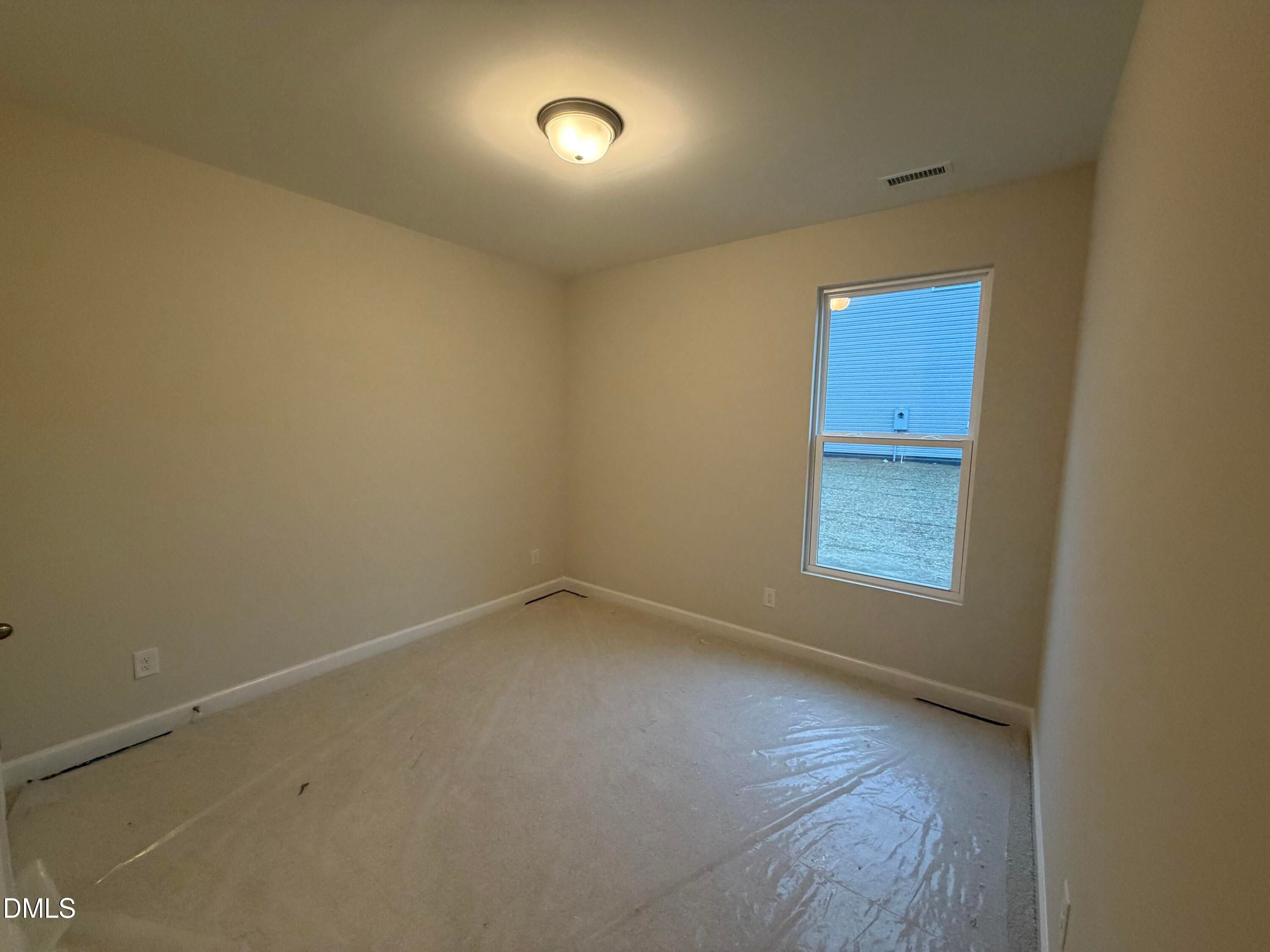 Spacious empty secondary bedroom with beige walls, large window, and protective flooring in The Daphne C home, Lillington, NC