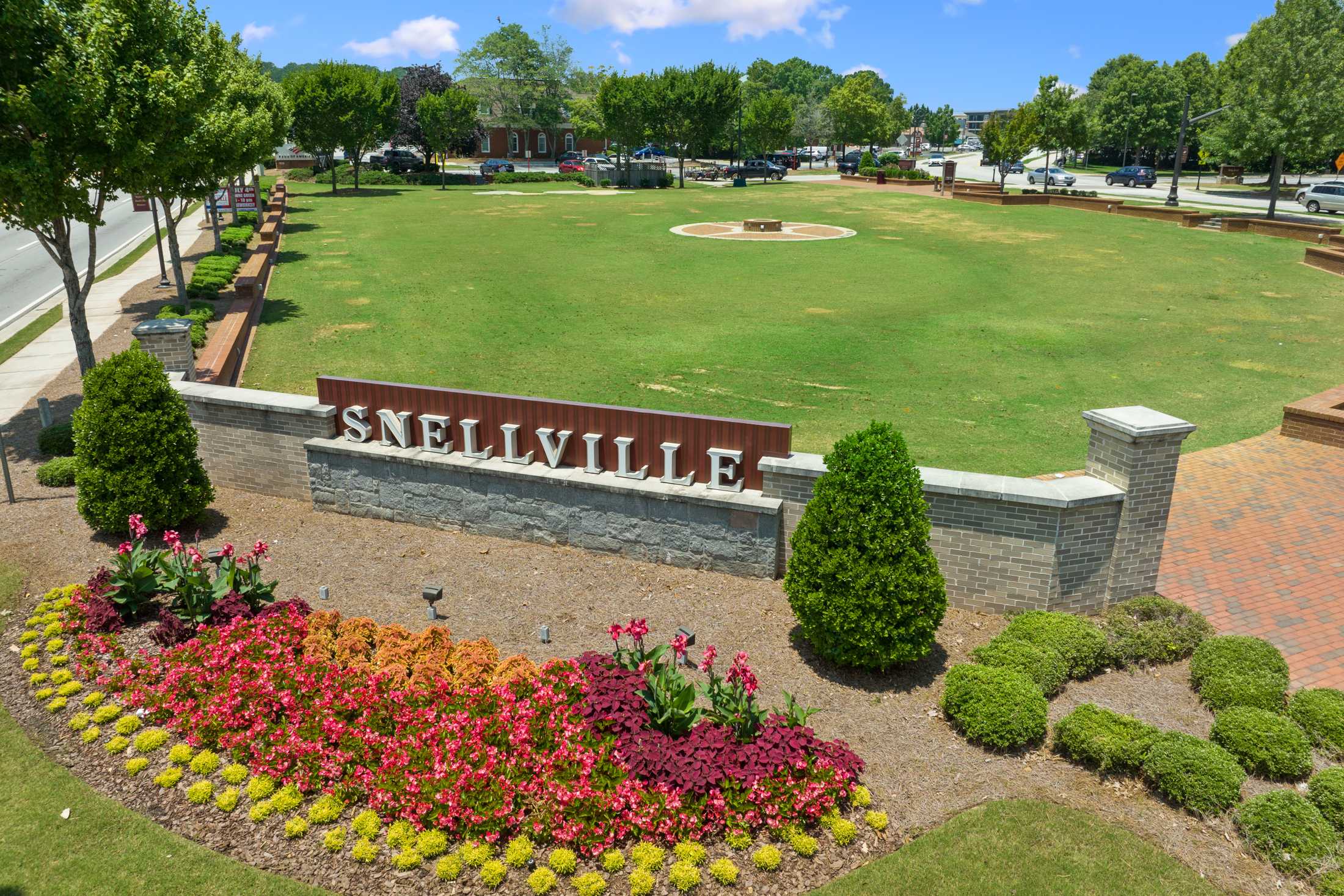 Landscaped Snellville welcome sign with stone lettering, vibrant red orange yellow flower beds, green turf, shrubs and trees in Georgia
