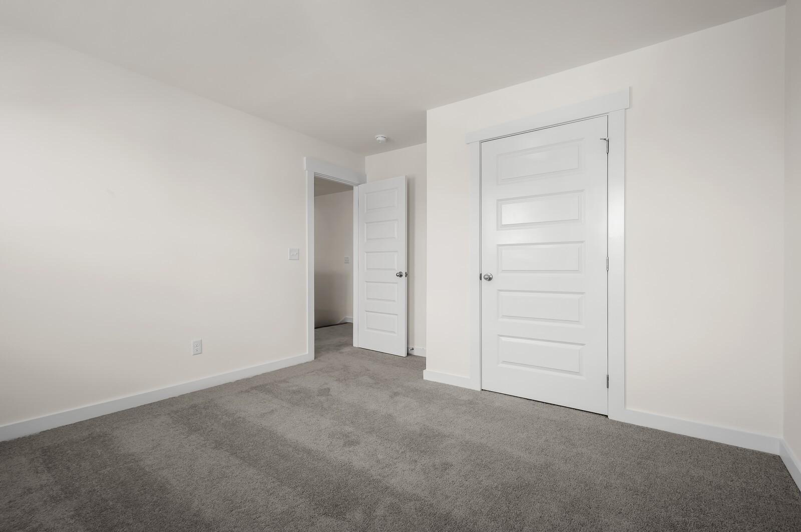 Bright bedroom with neutral carpet and white doors in The Ash A floor plan at Woods Crossing, Gallatin, Tennessee.