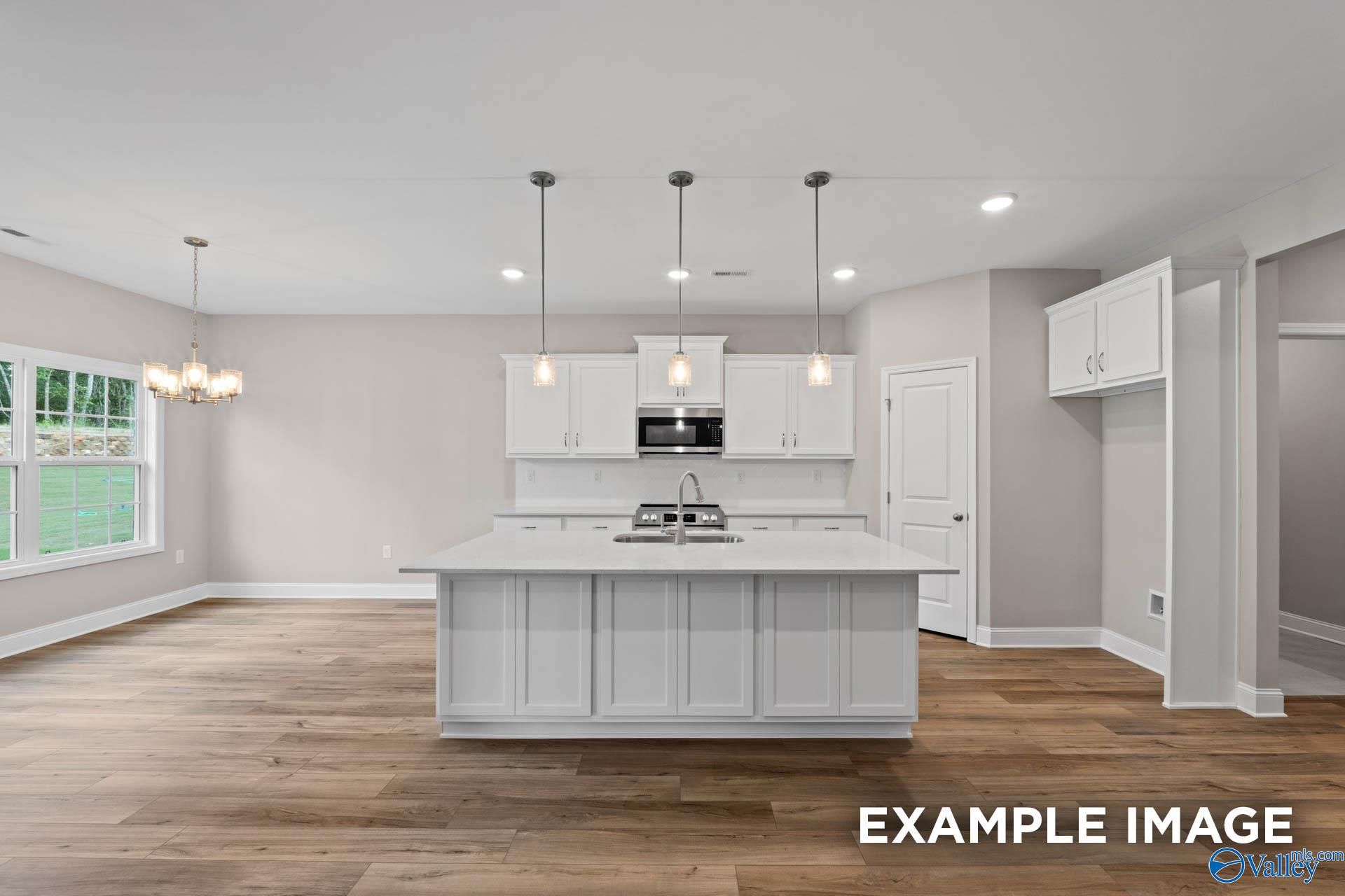 Bright modern kitchen with white shaker cabinets, large island sink, and open layout in The Montgomery 3-bedroom home, Meridianville, Alabama
